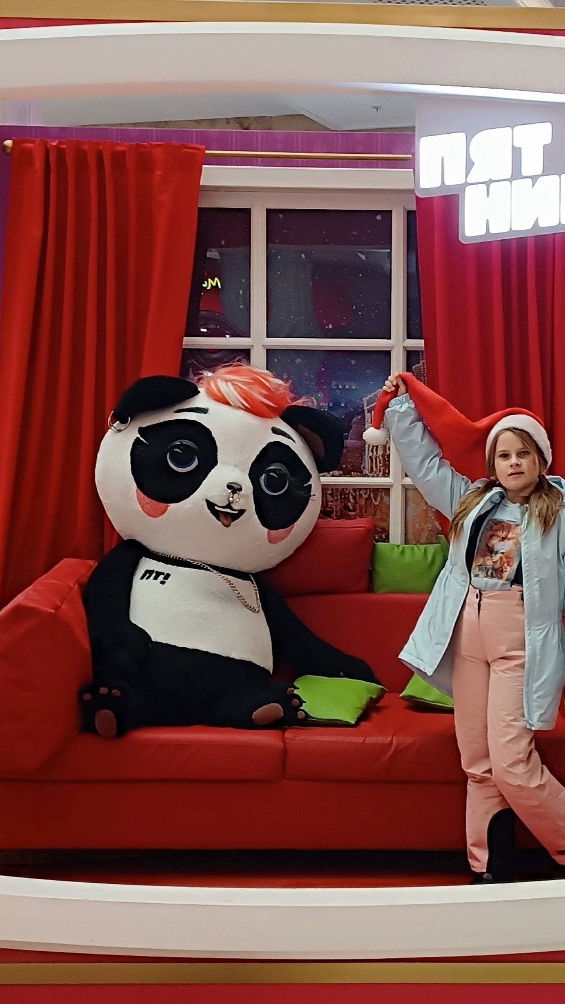 Giant panda mascot plush on a red sofa in a store photo zone, sewn to order for a TV channel
