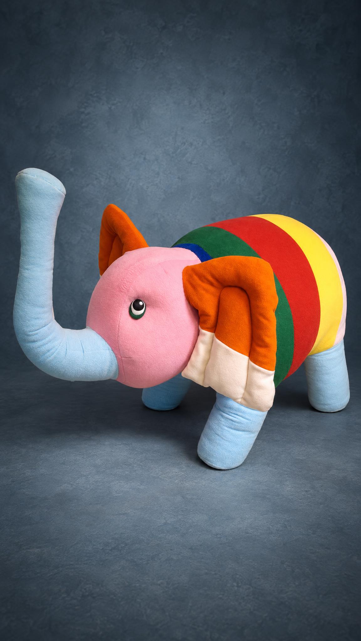 Rainbow-striped giant elephant plush with a raised blue trunk, handmade to order from a child's drawing