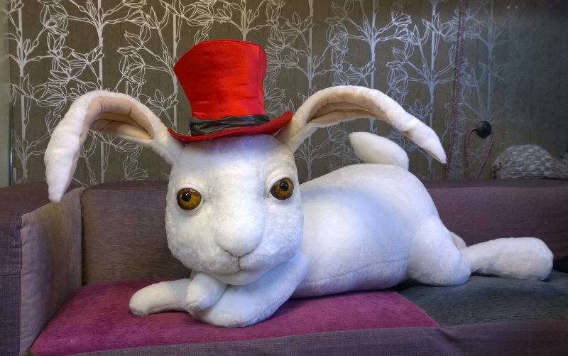 Giant white rabbit plush lying on a sofa Giant white rabbit plush handmade to order, lying across a sofa seat in a red top hat with a grey band