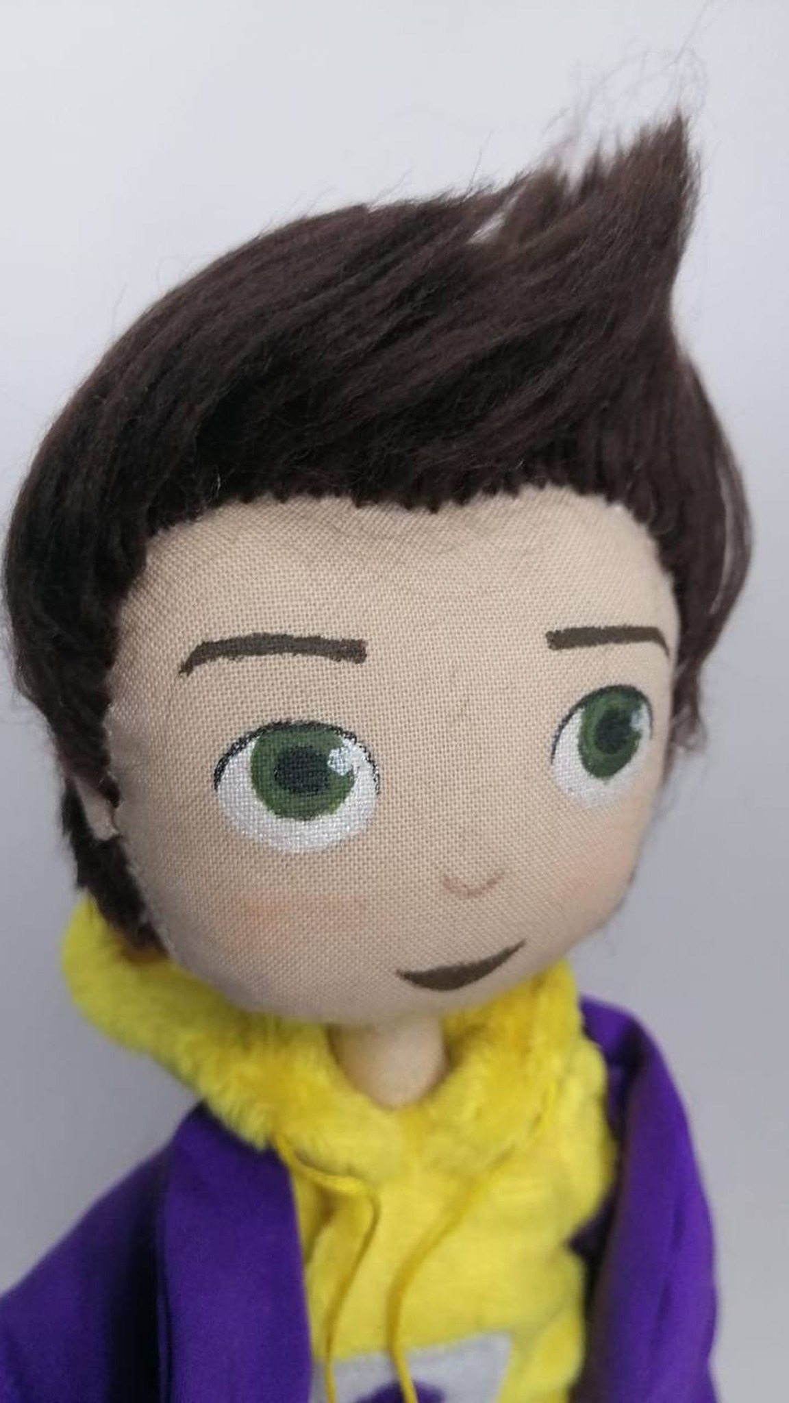 Painted fabric face of the graduate mascot doll with green eyes and a sideways smile, handmade to order