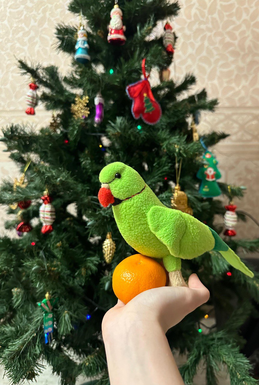 Green parrot plush by the New Year tree Handmade green parrot plush with a red beak on a hand by a New Year tree, custom ringneck made to order
