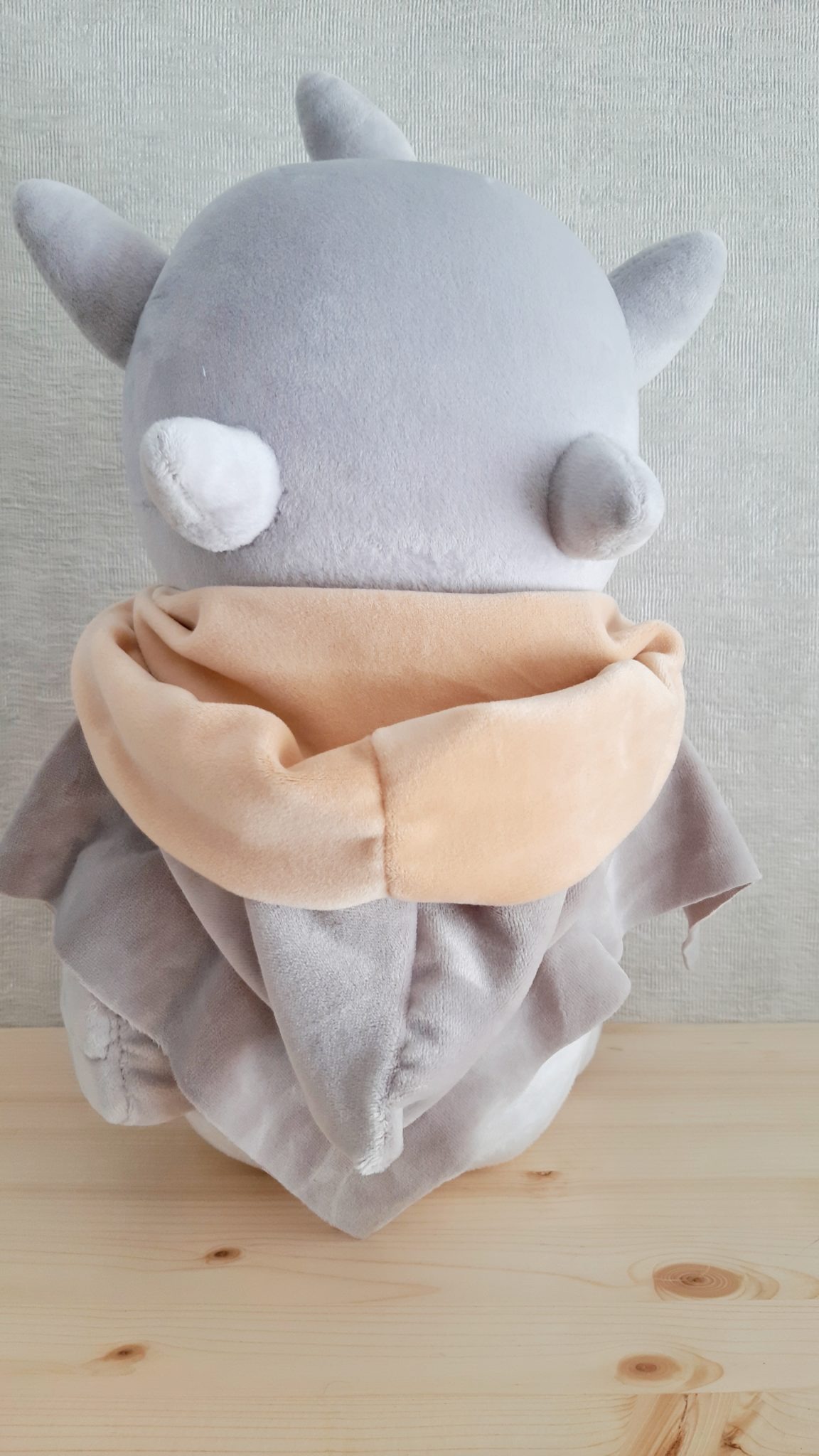 Grey monster plush with horns and small nubs on its head, peach scarf and draped grey cloak, sewn to order