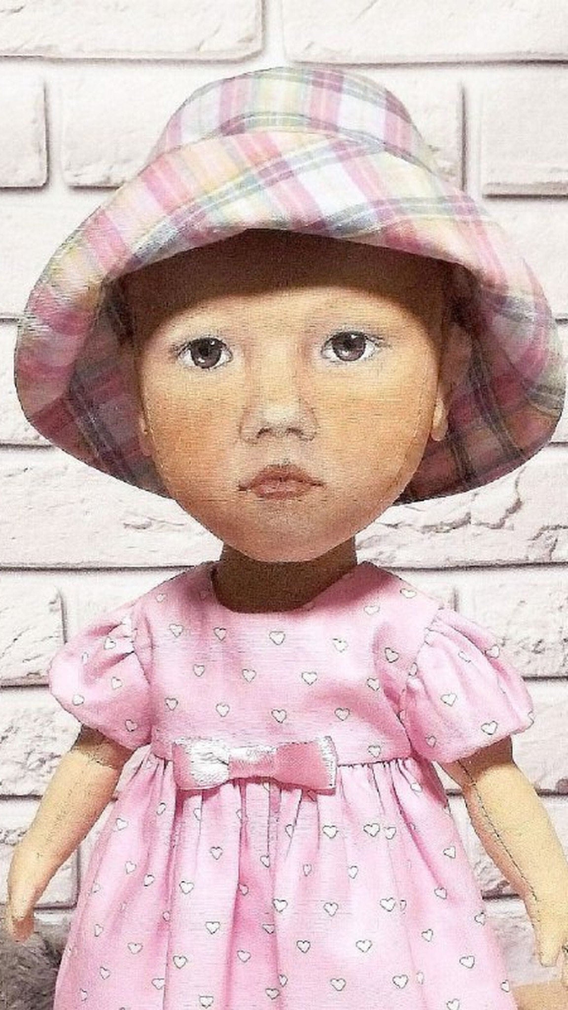 Hand-painted face of a custom baby doll: brown eyes, rosy cheeks, plaid sun hat, sewn to order from a photo