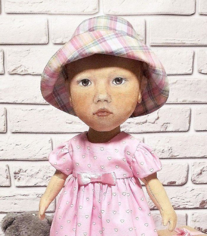 Hand-painted face of a toddler portrait doll Hand-painted face of a custom baby doll: brown eyes, rosy cheeks, plaid sun hat, sewn to order from a photo