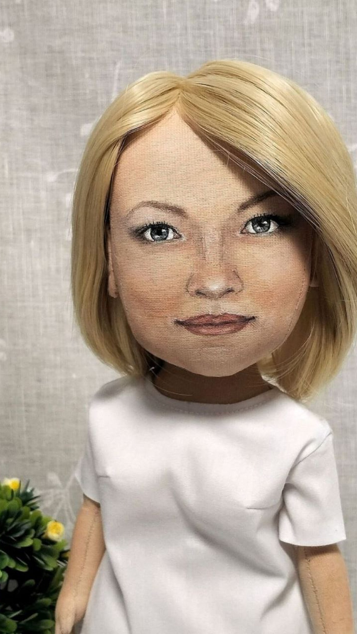 Hand-painted face of a custom portrait doll: grey-blue eyes, soft smile, blonde bob, sewn to order from a photo