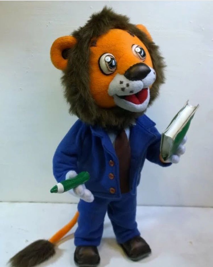 Company lion mascot plush with a tail tuft Company lion mascot plush standing in brown shoes with an orange tail and dark fur tuft, custom made by hand