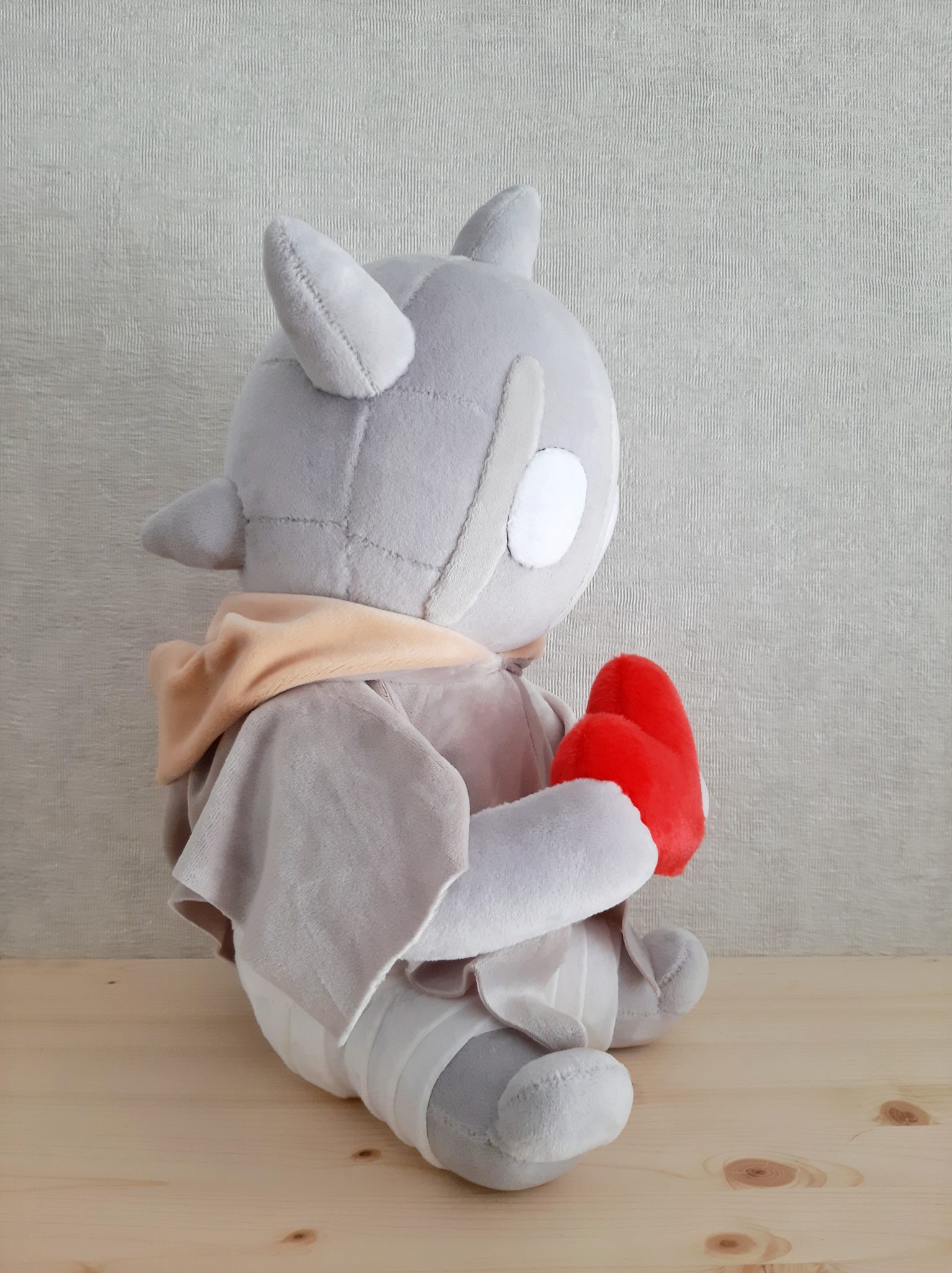 Horned monster plush with a red heart Horned monster plush in a grey cloak clutching a red heart, mask-like stitched face and white eye, custom made