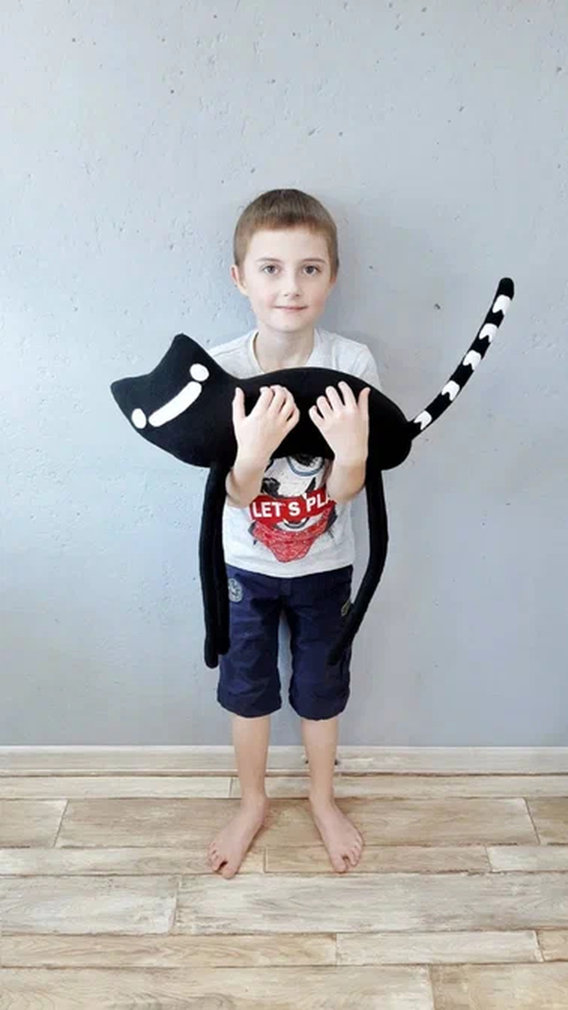 Boy holding the long-legged black cat plush across his chest to show its size, sewn to order from a drawing