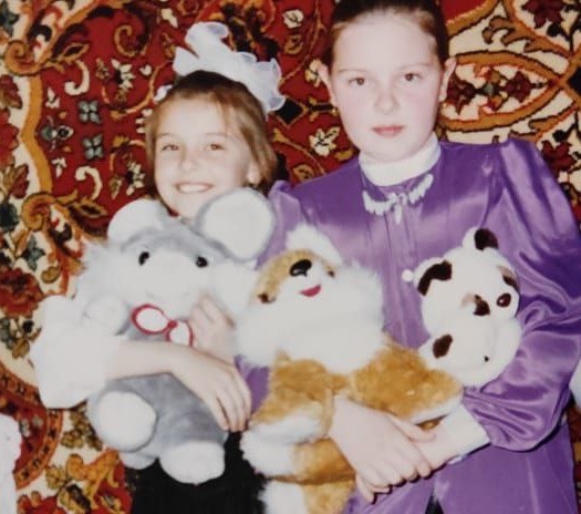 Childhood photo of the original bunny with other toys Second old family photo: the younger girl holding her gray bunny with a red-and-white bow among other toys