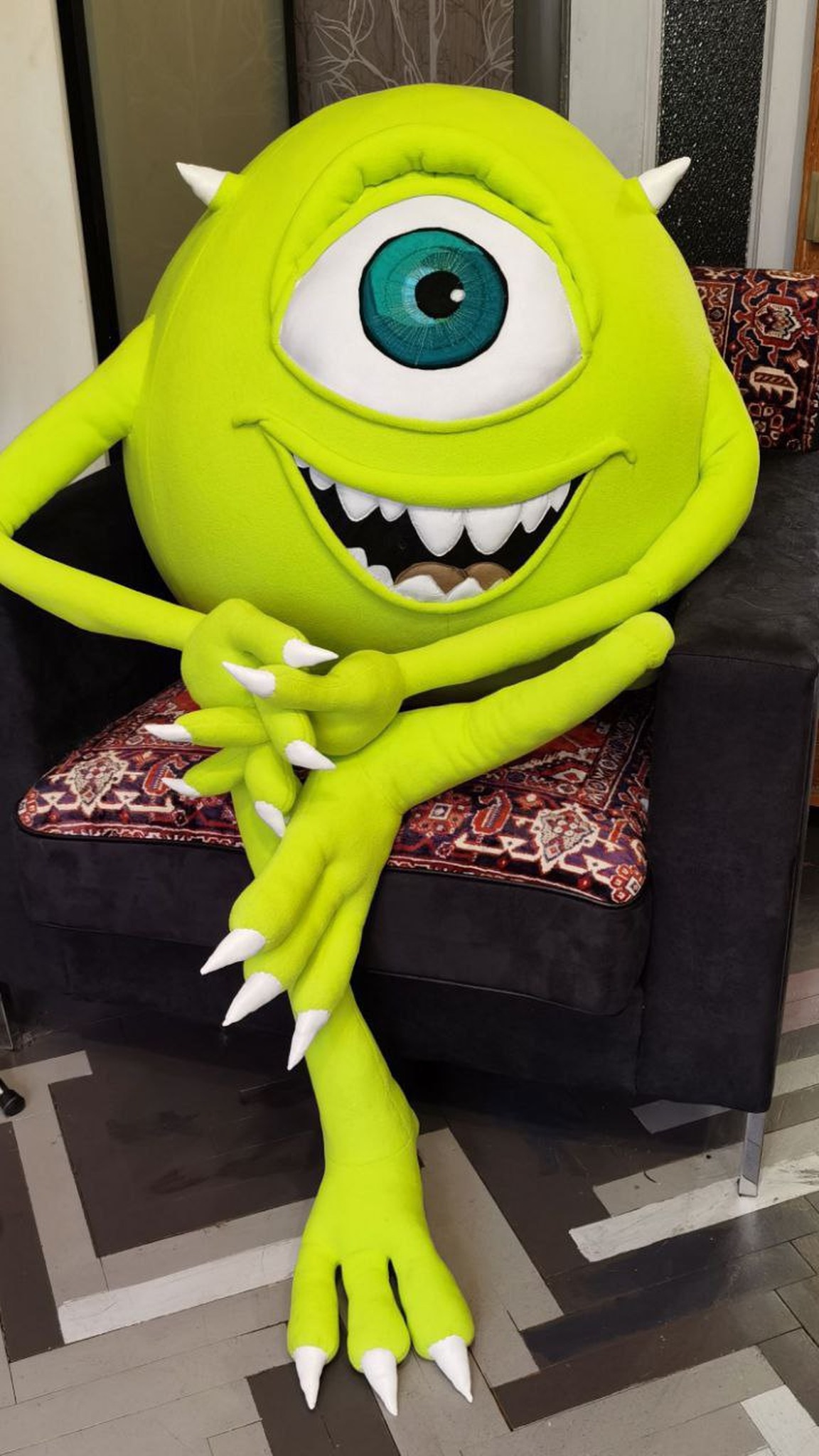 Custom Mike Wazowski plush sitting in an armchair, long green legs and white claws reaching the floor