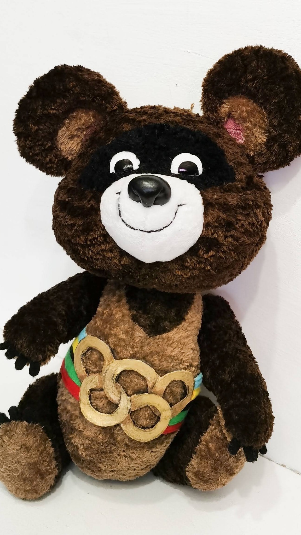 Olympic Misha plush sewn to order, sitting: black mask, glossy nose, gold rings on a rainbow belt