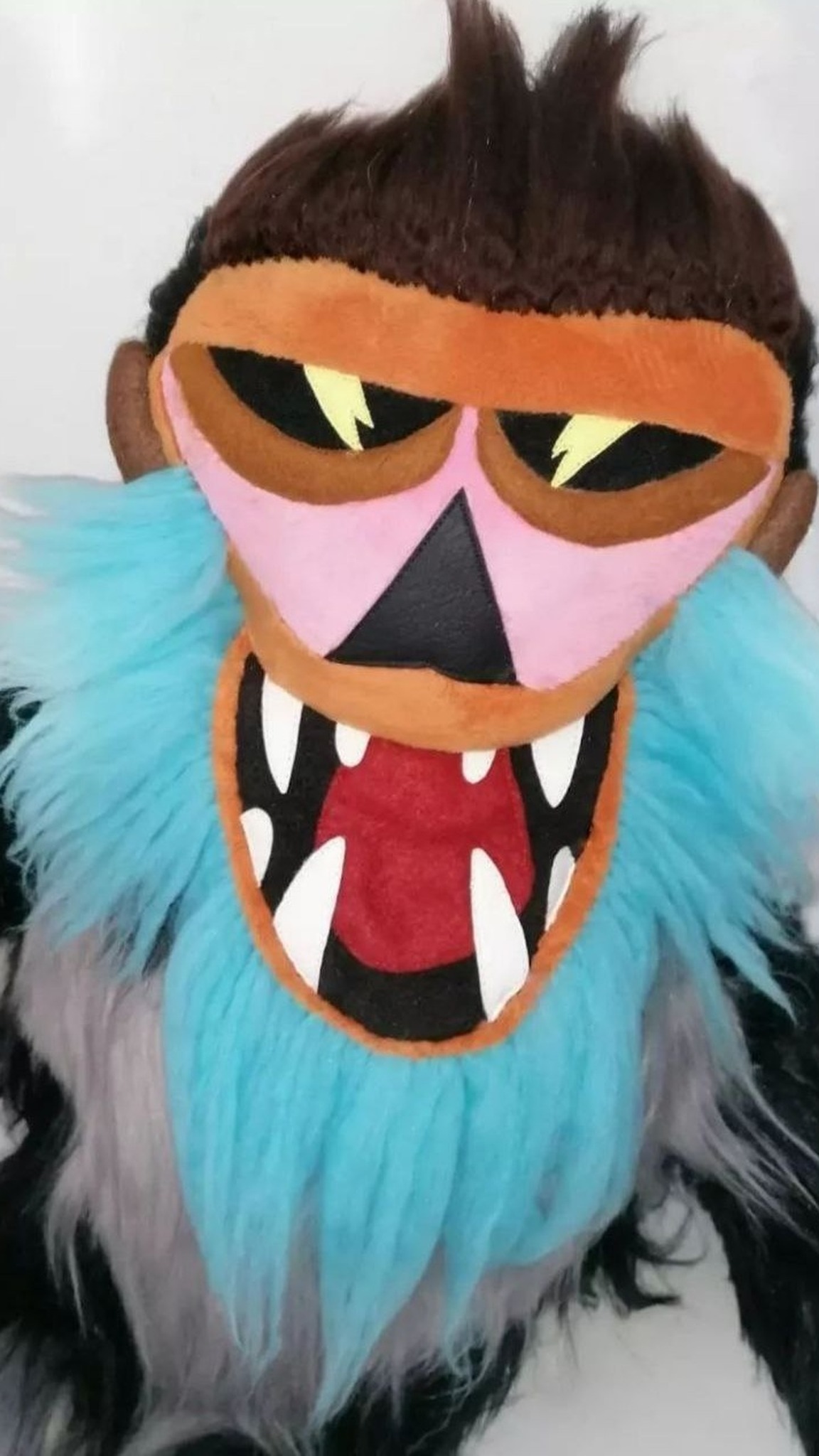 Lightning-bolt eyes, black triangle nose and fanged grin on a custom monkey mascot plush sewn from a logo