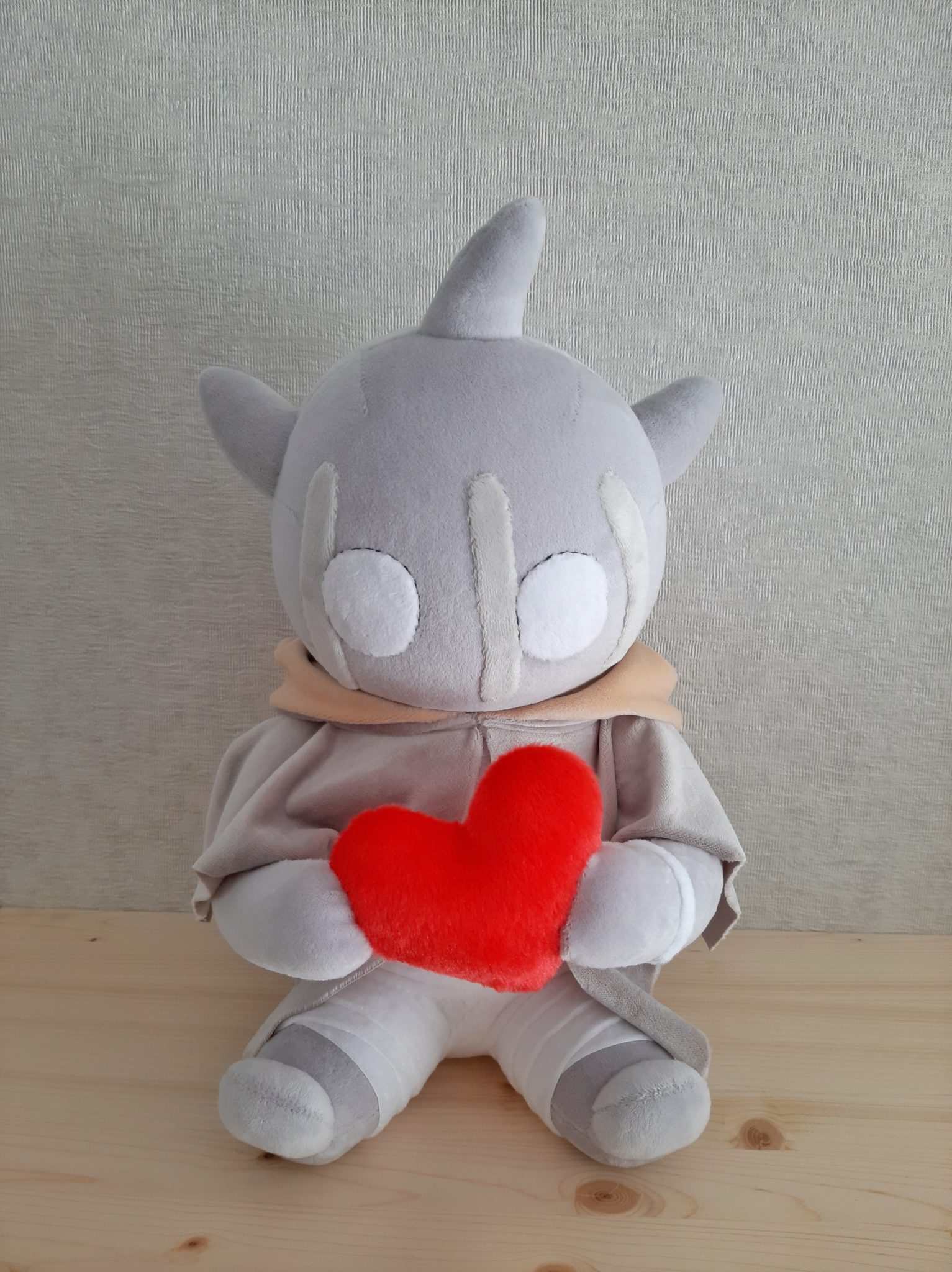 Monster plush with a heart, handmade Monster plush with a red heart sitting on a wooden table, grey horns, peach scarf and banded legs, handmade