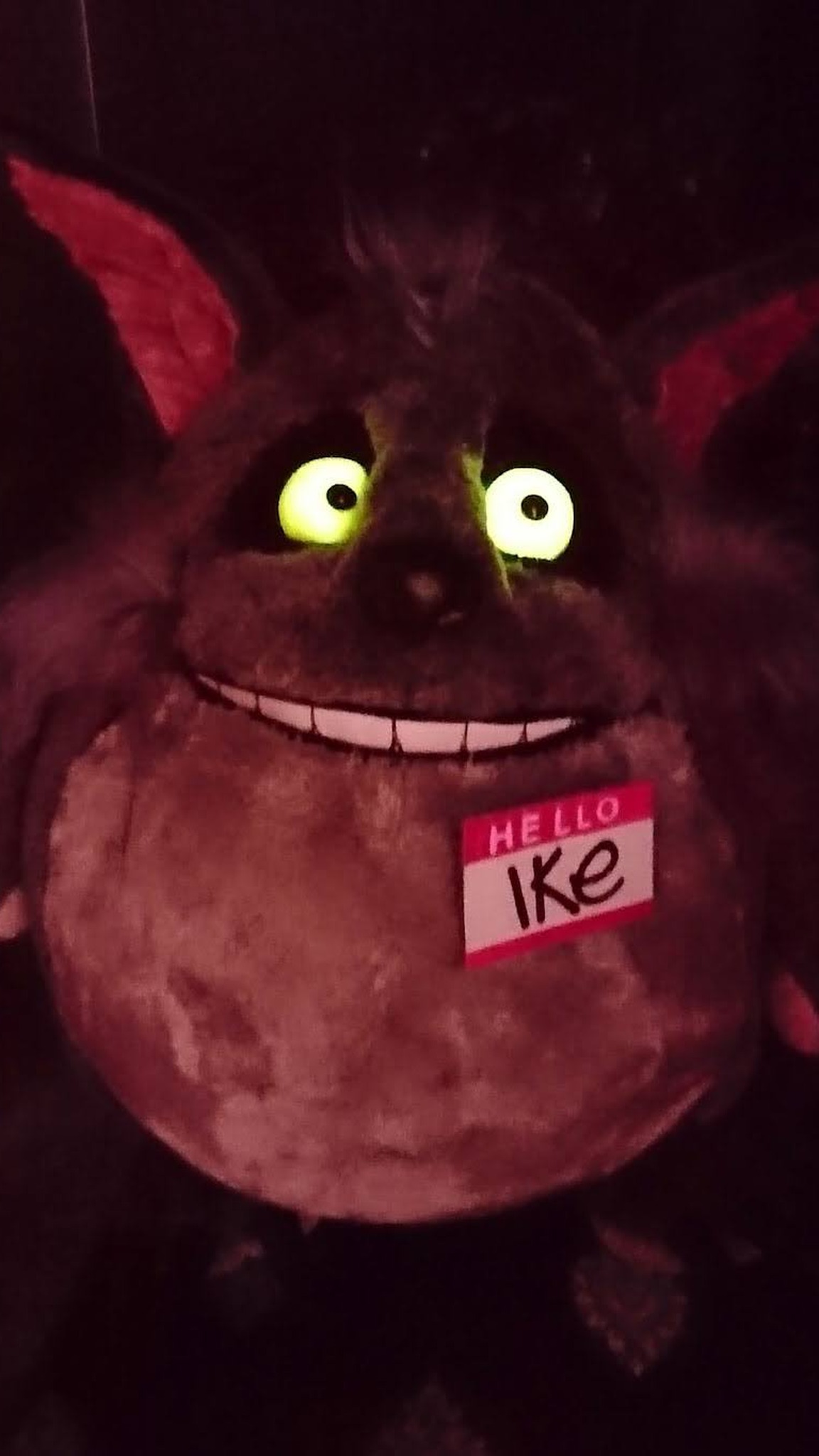 Monster wolf plush Ike with glowing eyes in a dark room, grey faux fur and name badge, custom made