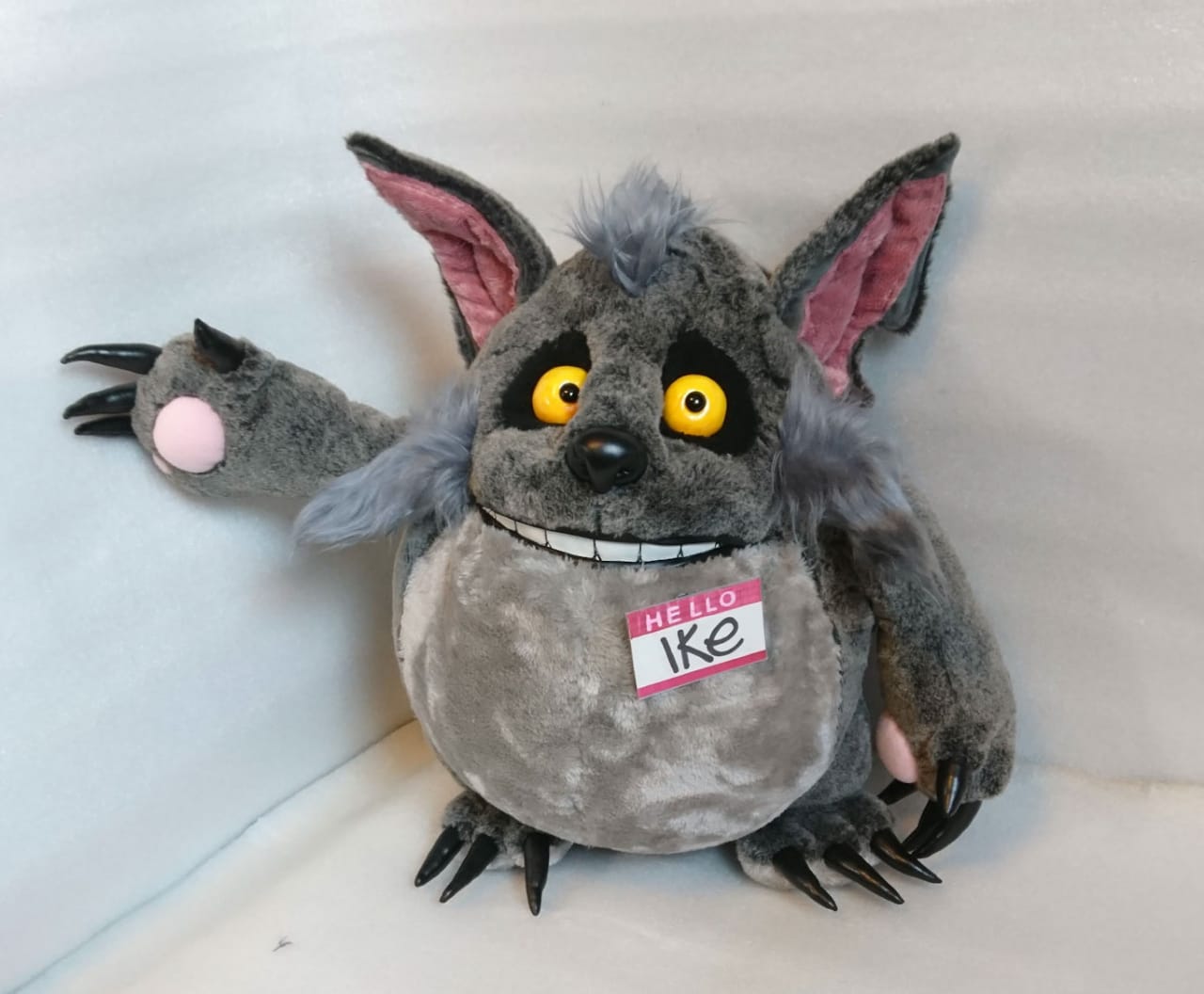 Monster wolf plush with a raised clawed paw Monster wolf plush raising a clawed hand with a pink palm pad, grey faux fur and HELLO Ike badge, custom made