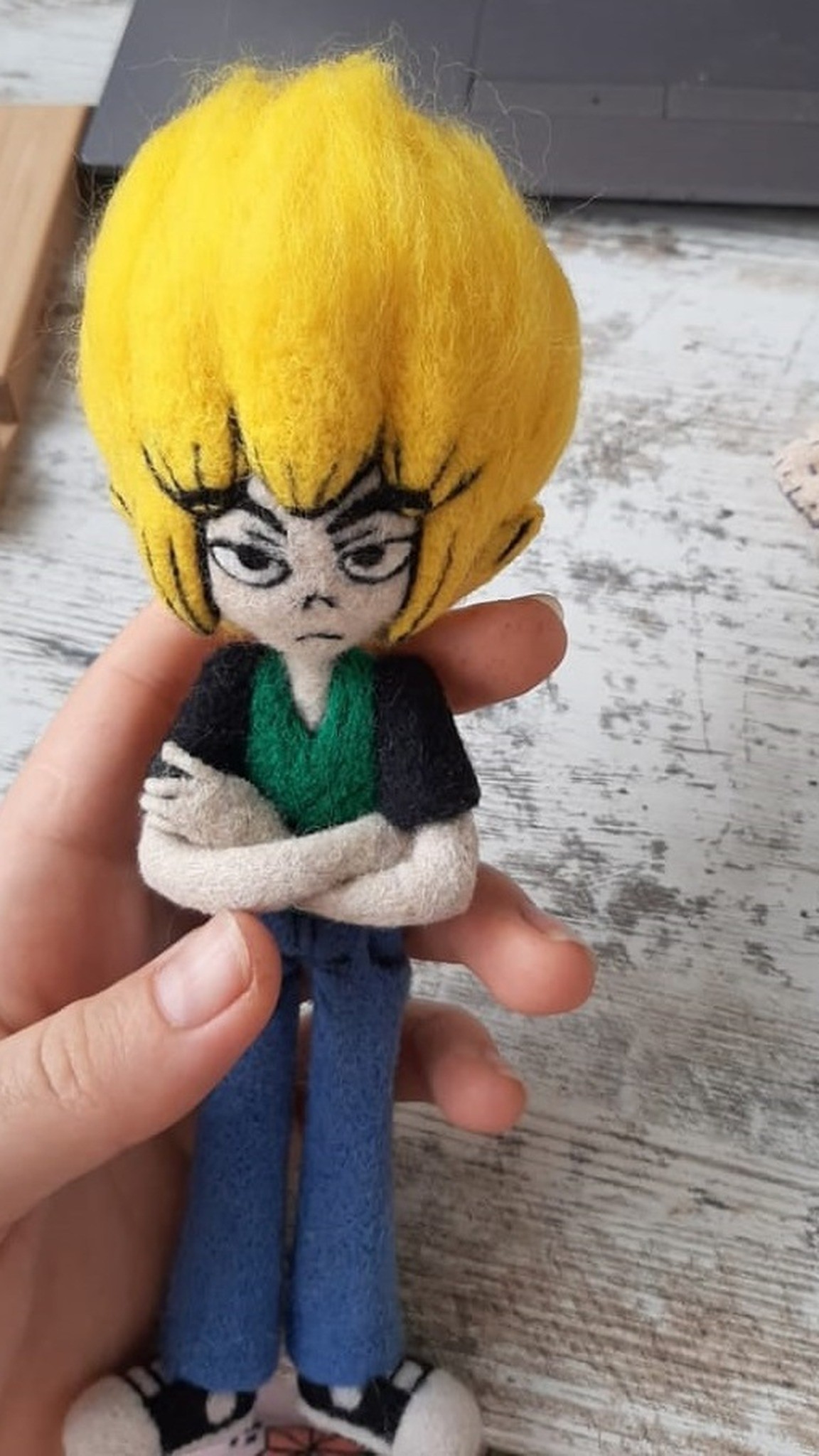 Small needle felted anime doll held in one hand, grumpy face with fine black brows and eyes, handmade