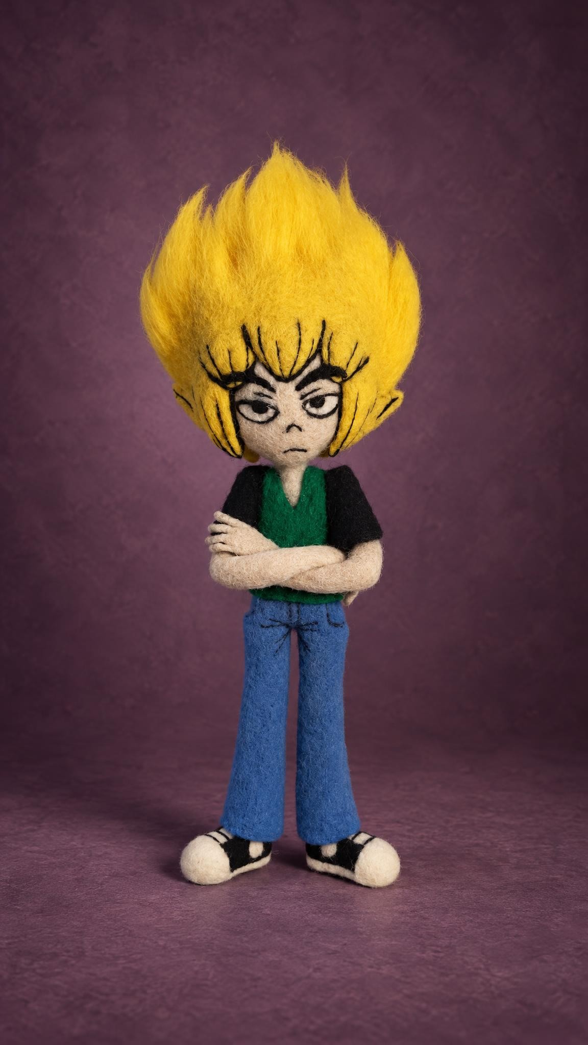 Felted anime boy doll in a black shirt, green top and blue trousers, arms crossed, handmade to order