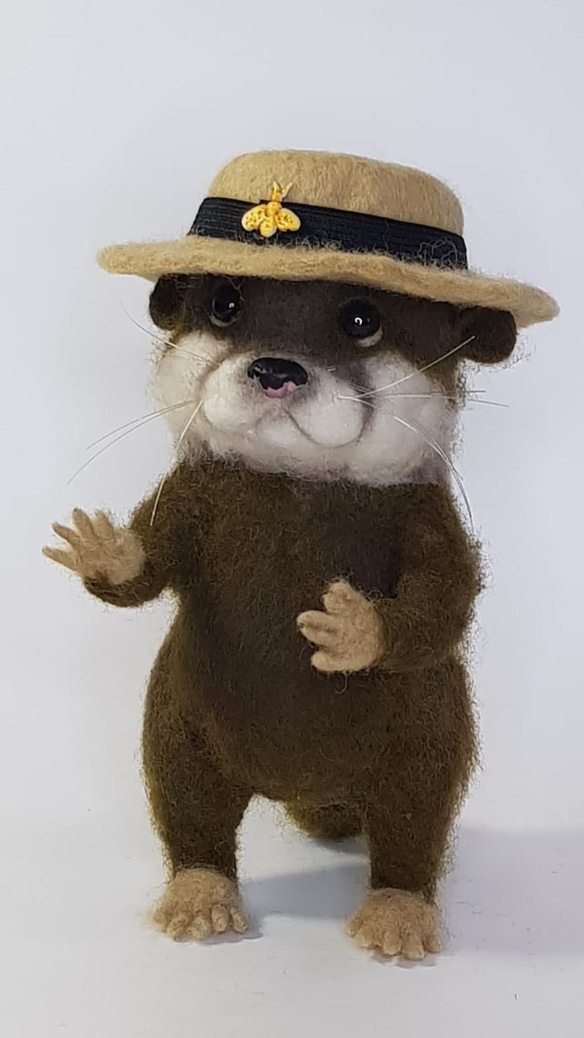 Needle felted otter plush waving a paw under a beige boater with a gold bee, handmade to order