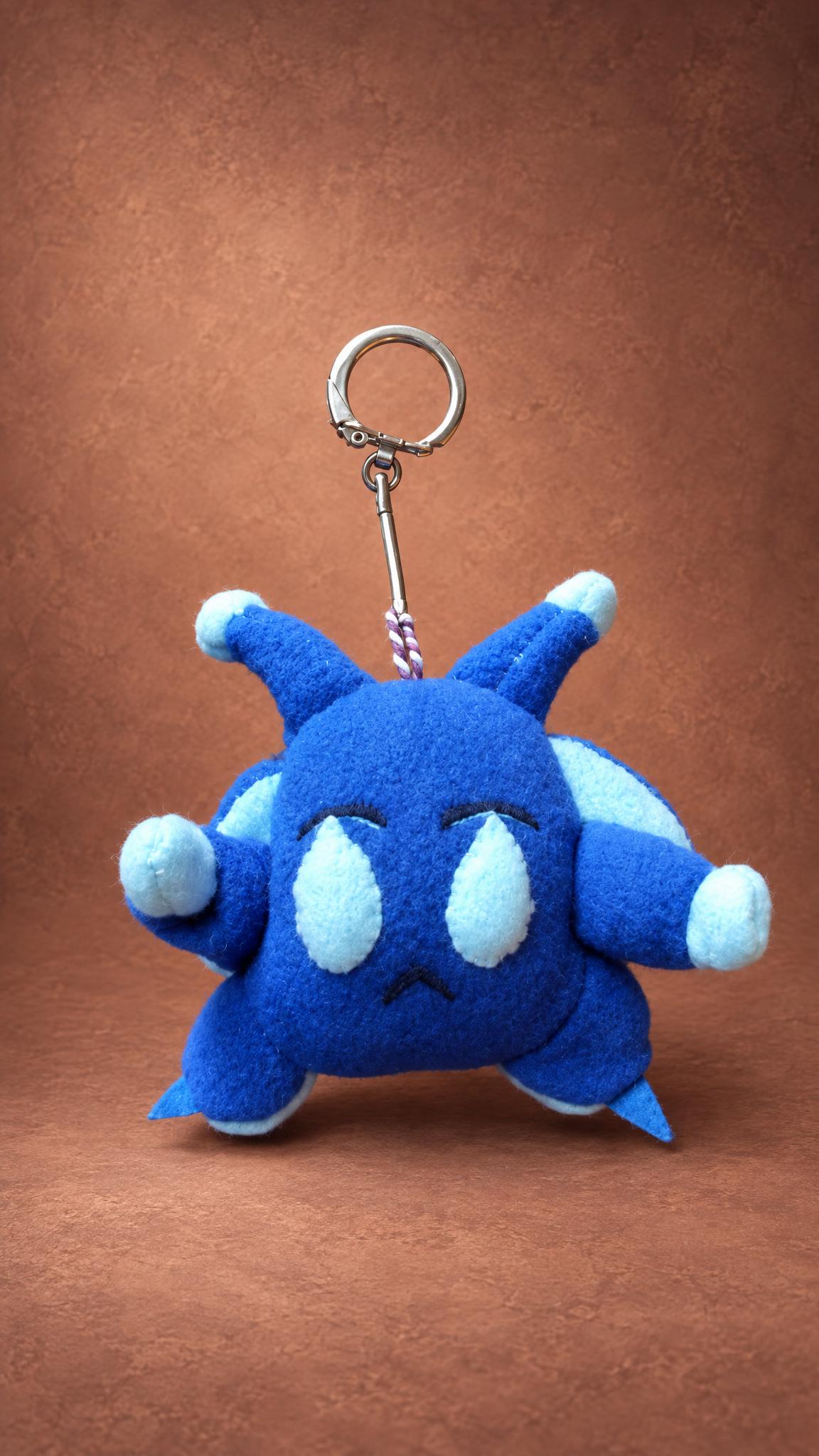 Custom plush keychain of a blue clay monster with a frown and pale-blue paws, sewn by hand to order
