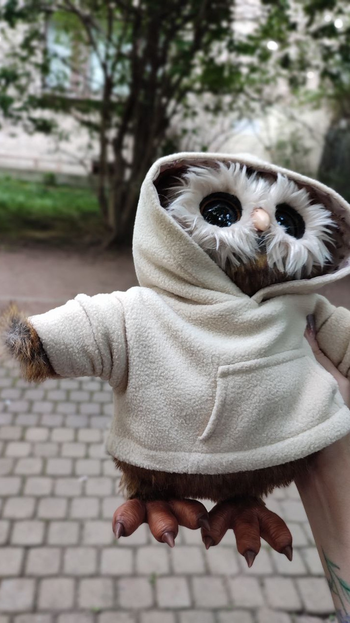 Custom owl plush with the hood pulled up over his ear tufts, held in one hand, brown toes and dark claws