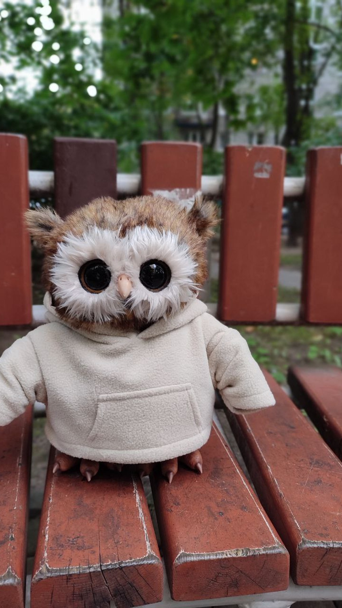 Handmade owl plush in a cream hoodie sitting on a red park bench, faux fur ear tufts and big dark eyes