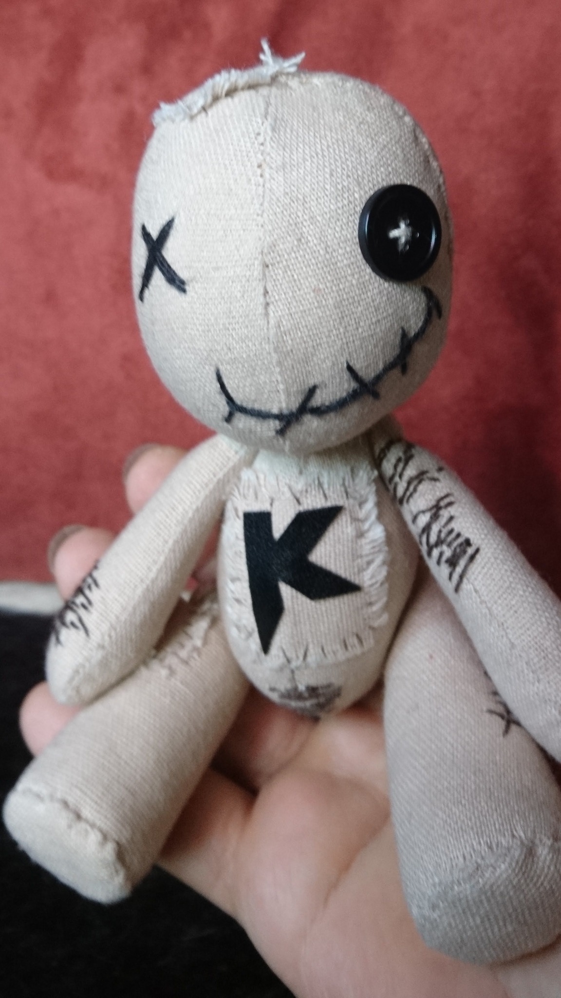 Small custom voodoo doll in a hand, cream canvas with stitch scars and a black K, sewn to order