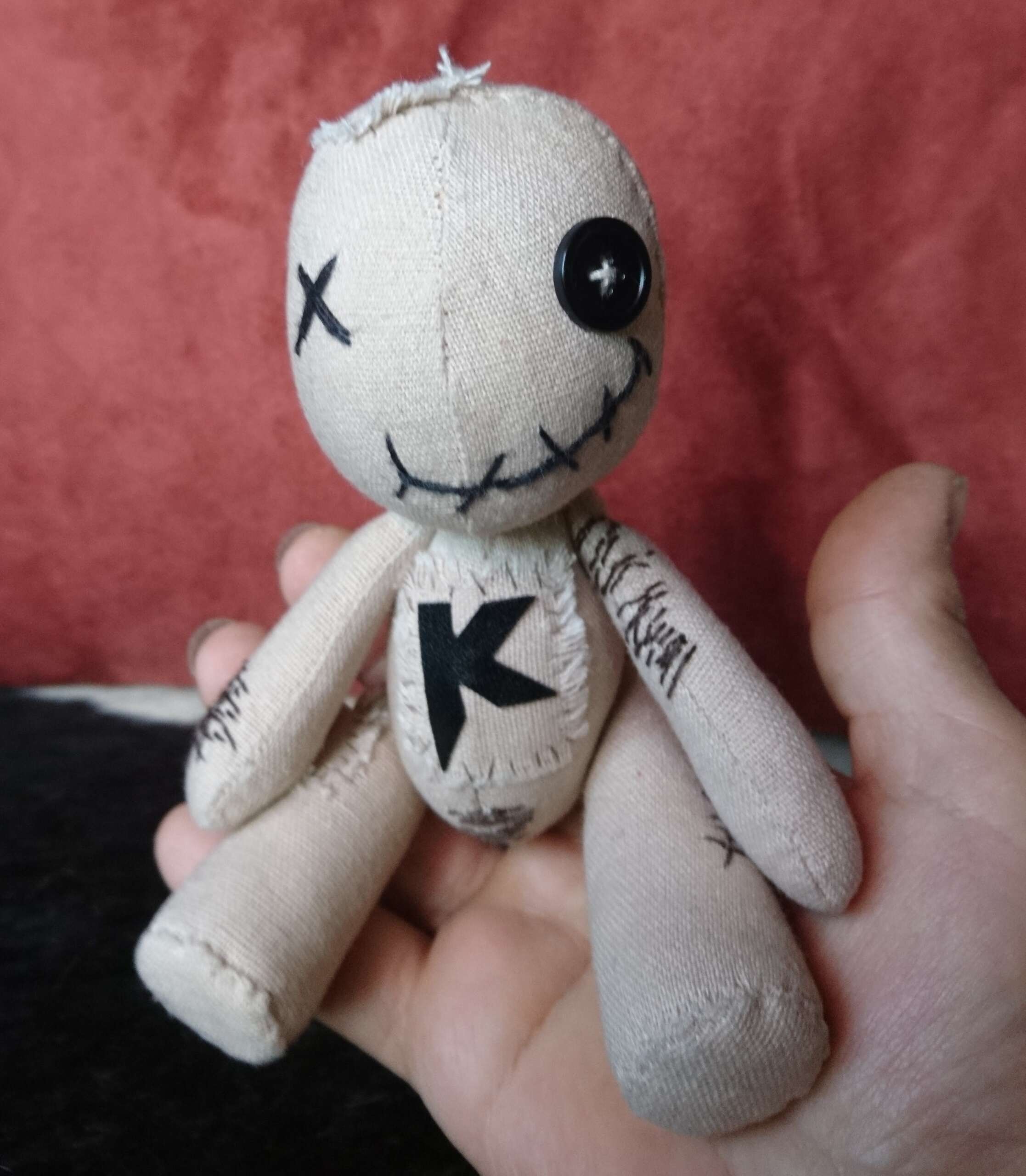 Palm-size voodoo doll plush Palm-size voodoo doll plush with a button eye, stitched smile and a bold K, sewn by hand to order