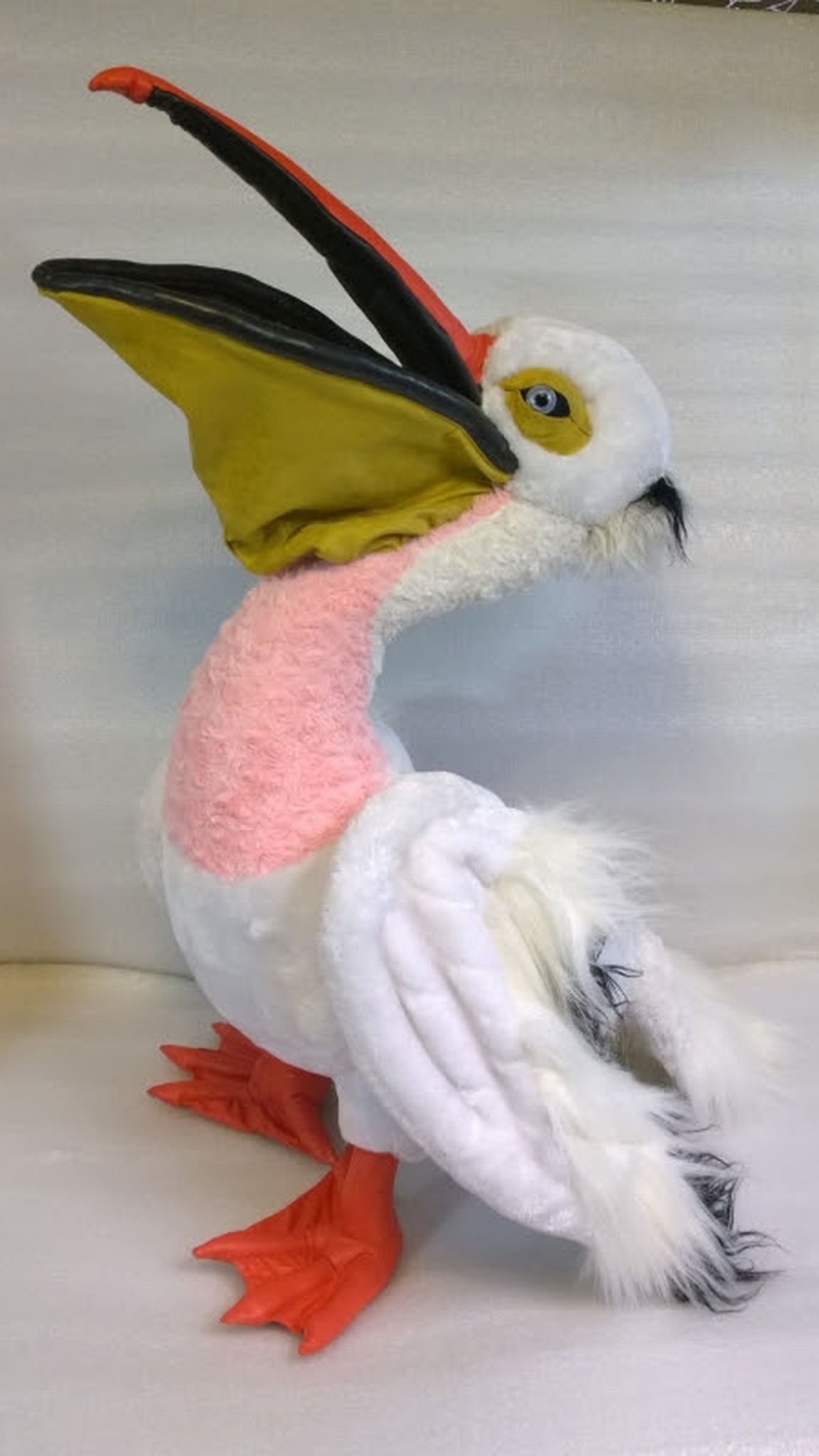 Pelican plush pointing its open beak up, mustard pouch and pink chest, white faux fur wings, made to order