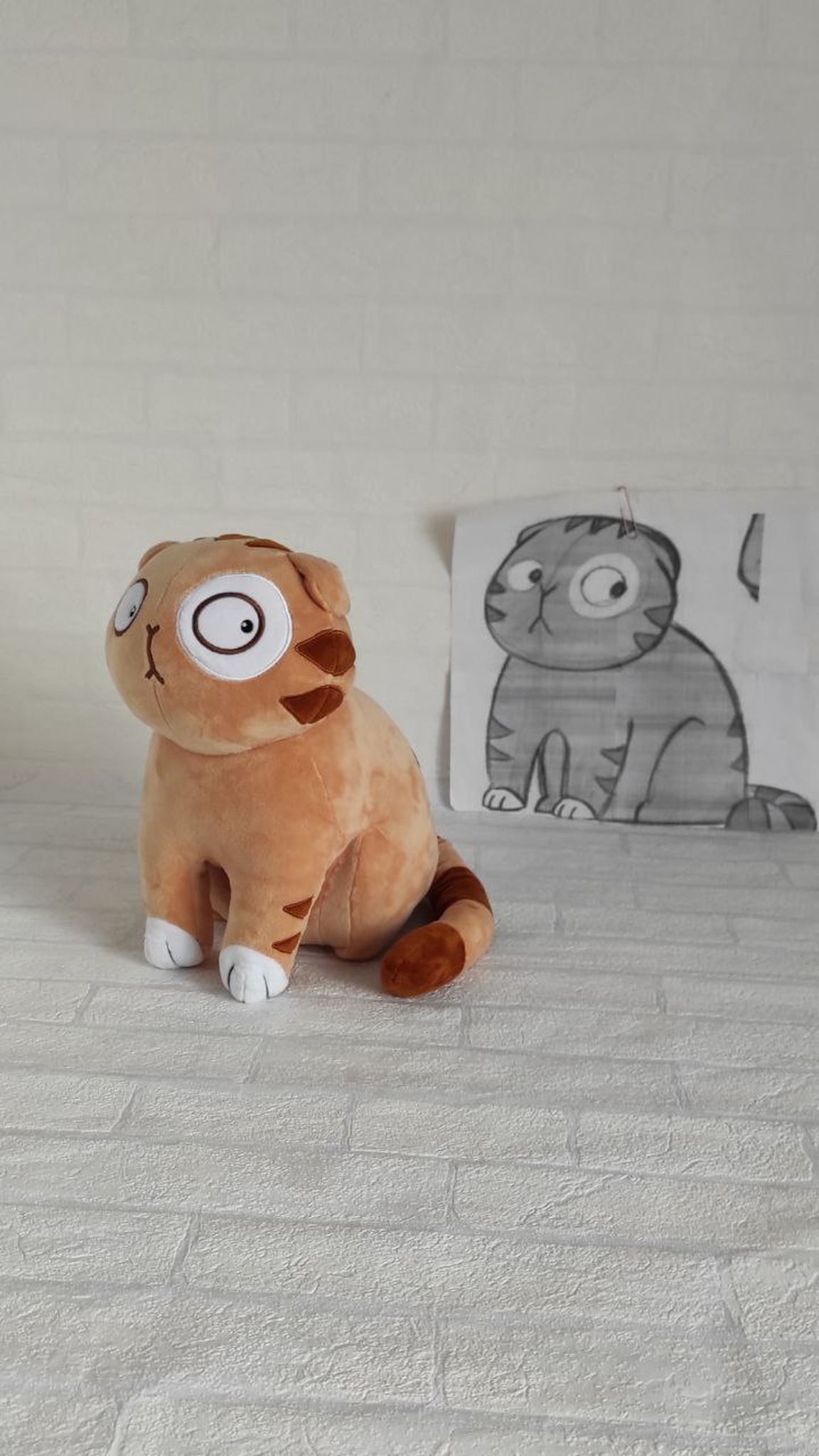 Persik cat plush made to order from a sticker, sitting next to a printed drawing of the same cat