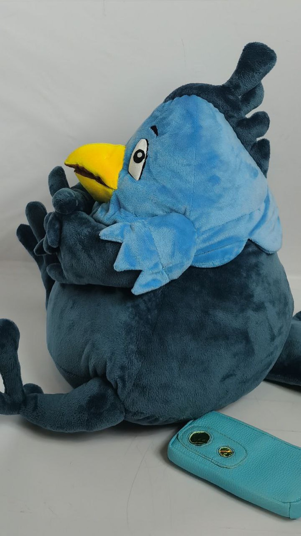 Phoenix mascot plush with a feathered crest and a light blue collar, its phone set down beside it, made to order