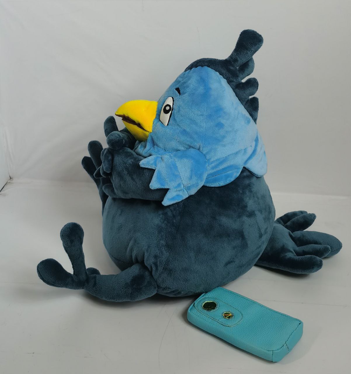 Phoenix mascot plush with a crest Phoenix mascot plush with a feathered crest and a light blue collar, its phone set down beside it, made to order