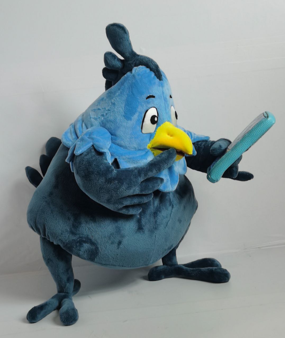 Phoenix mascot plush reading on its phone Phoenix mascot plush reading on its phone, a custom bird plush with a scalloped blue collar, sewn to order