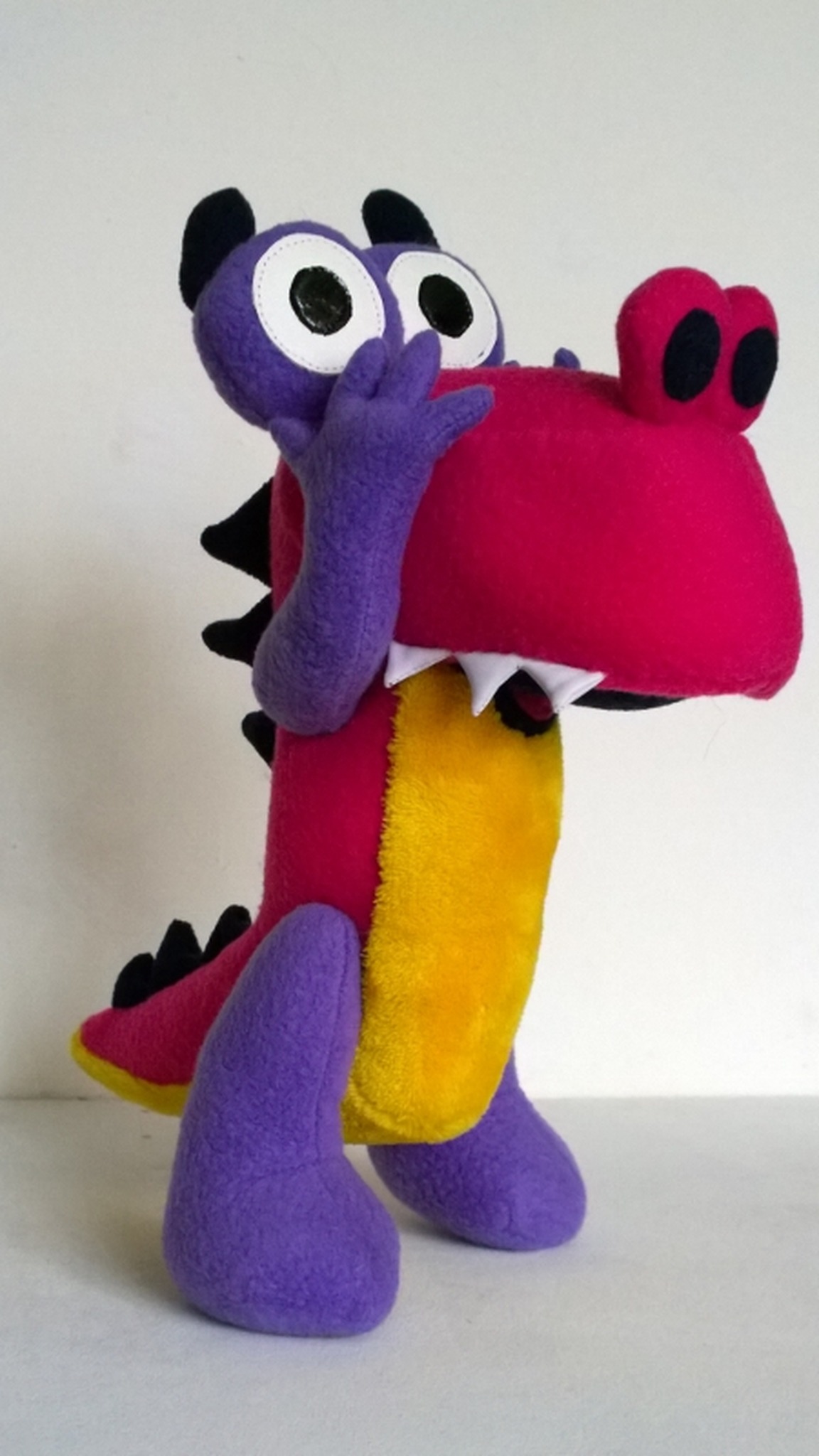 Pink dinosaur plush Grisha from Zavriki with a yellow tummy, white teeth and a hand at his face, custom made