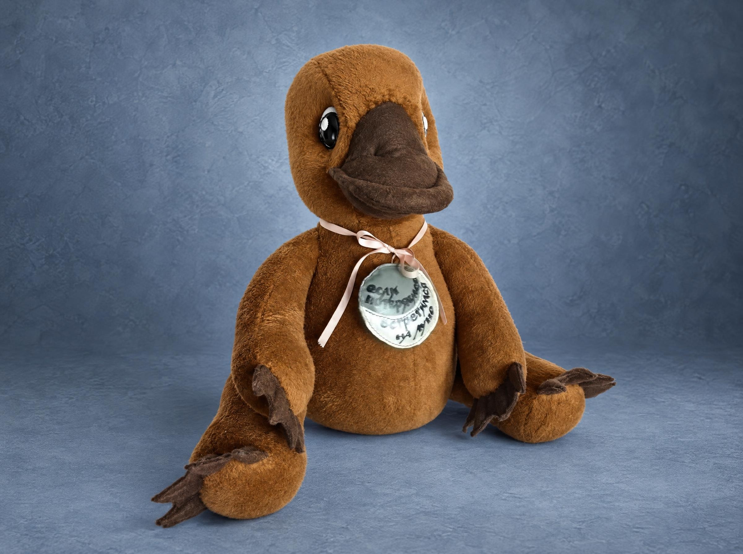 Custom platypus plush in warm brown with a dark bill and a silver medal on a pink ribbon, made to order