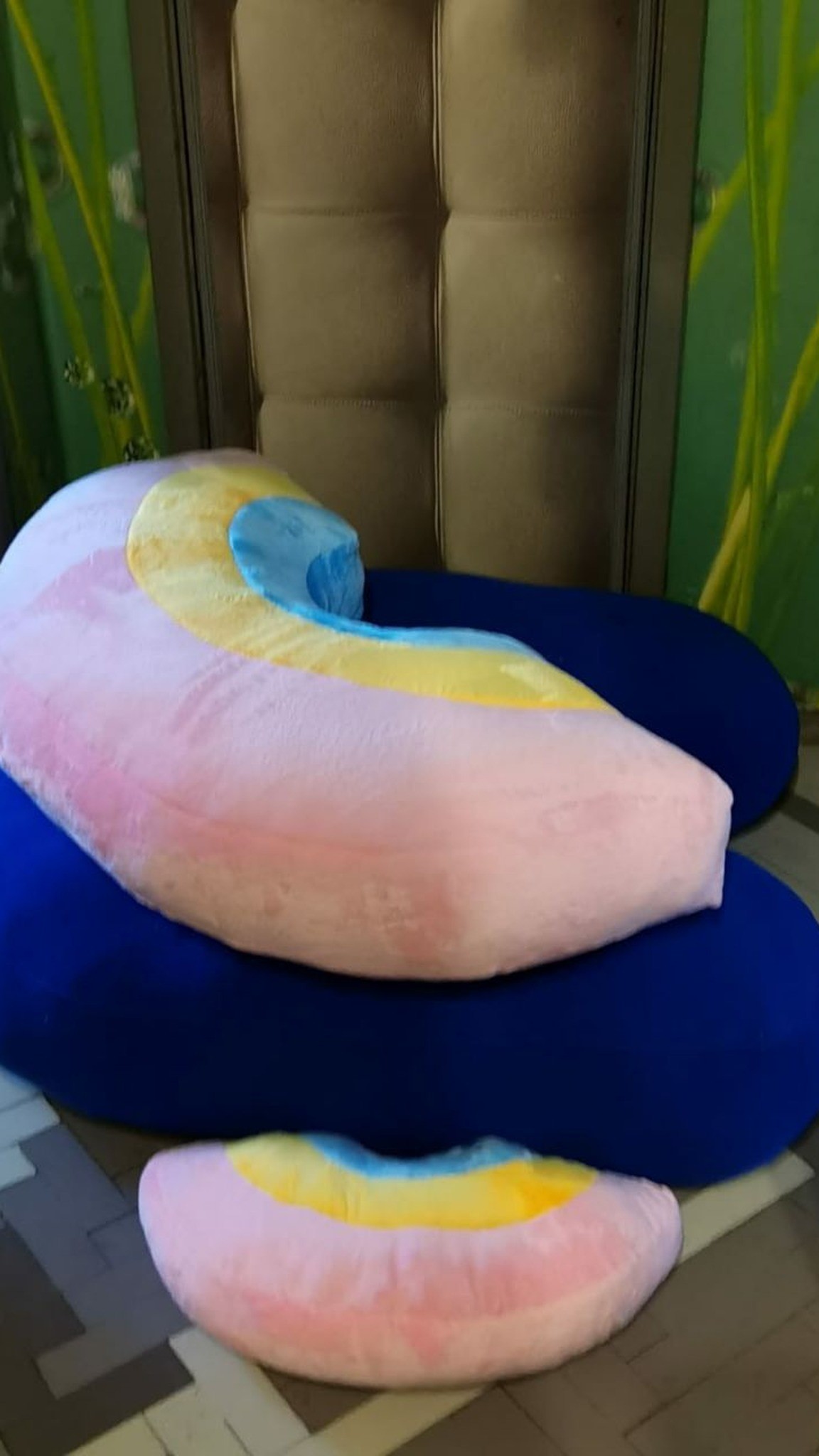 Two plush rainbows resting on giant blue plush logo letters, soft brand decor sewn to order