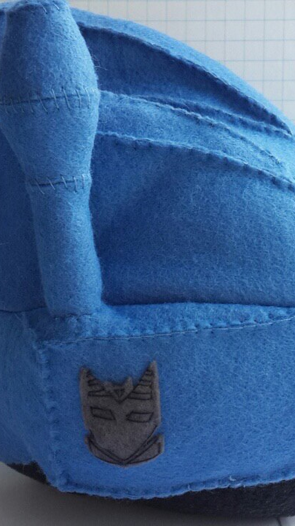 Grey felt Decepticon badge stitched on the blue helmet of a handmade Puggleformer Transformers plush
