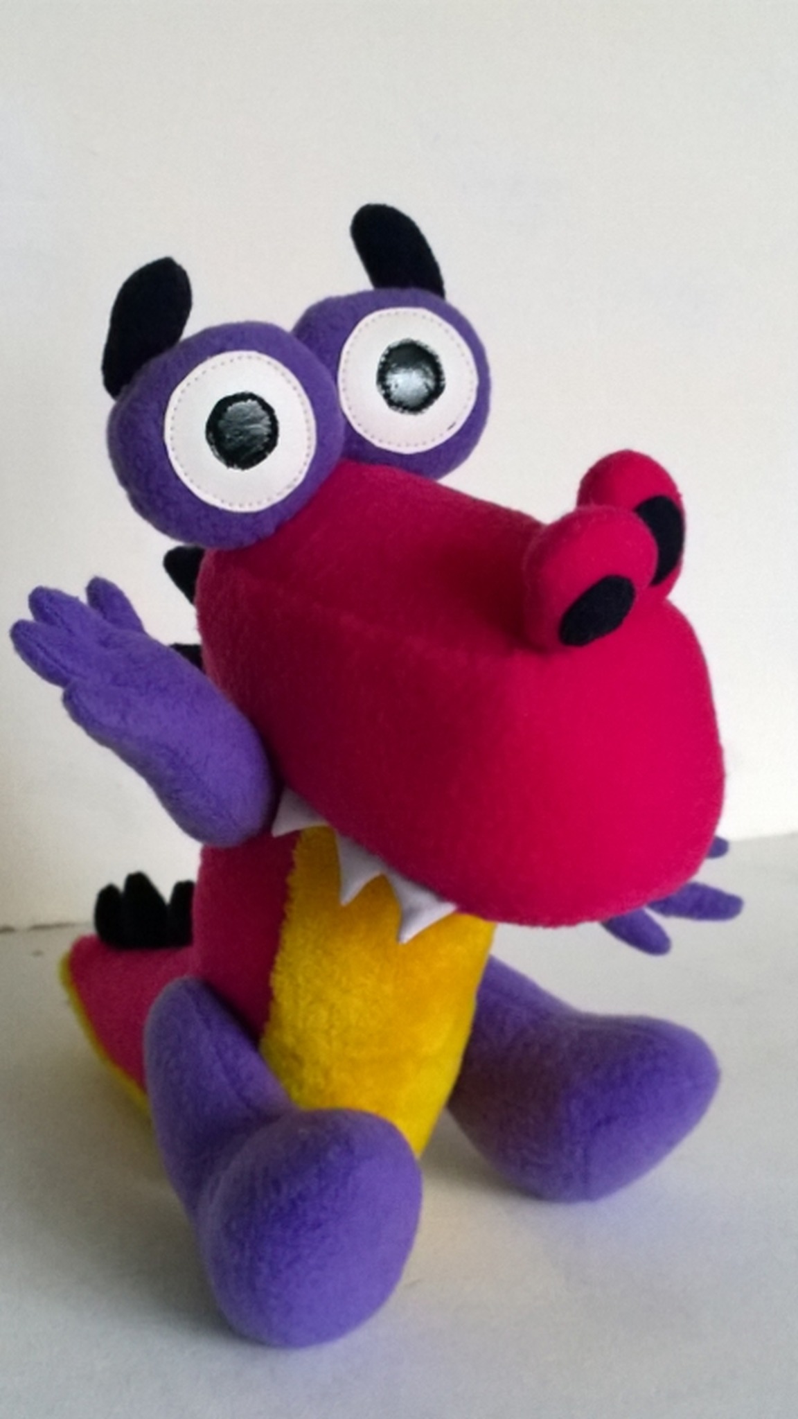 Purple and pink Zavriki dinosaur plush waving a three-finger hand, big white eyes and black horns, handmade