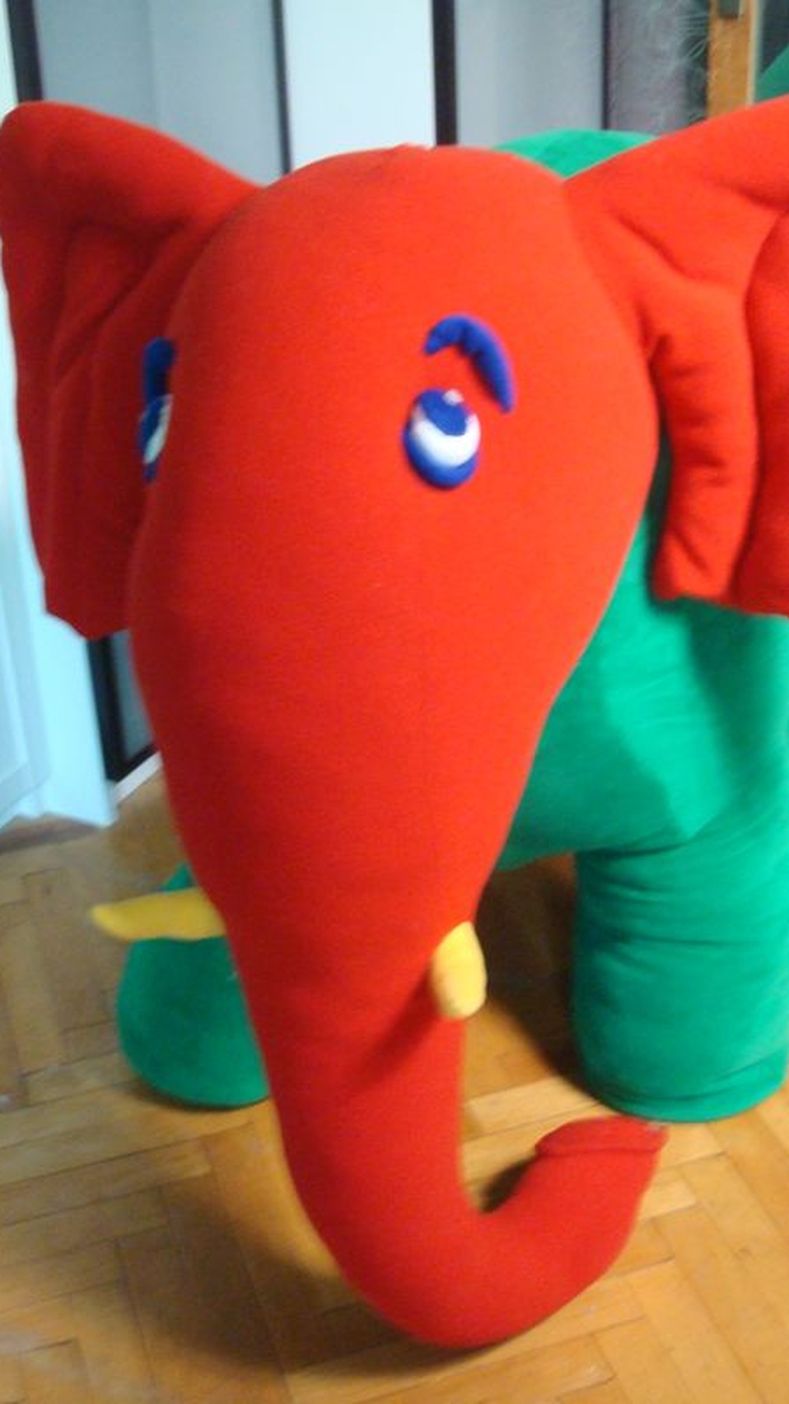 Red and green elephant plush with blue appliqué eyes, raised brows and yellow tusks, custom made from kids' art