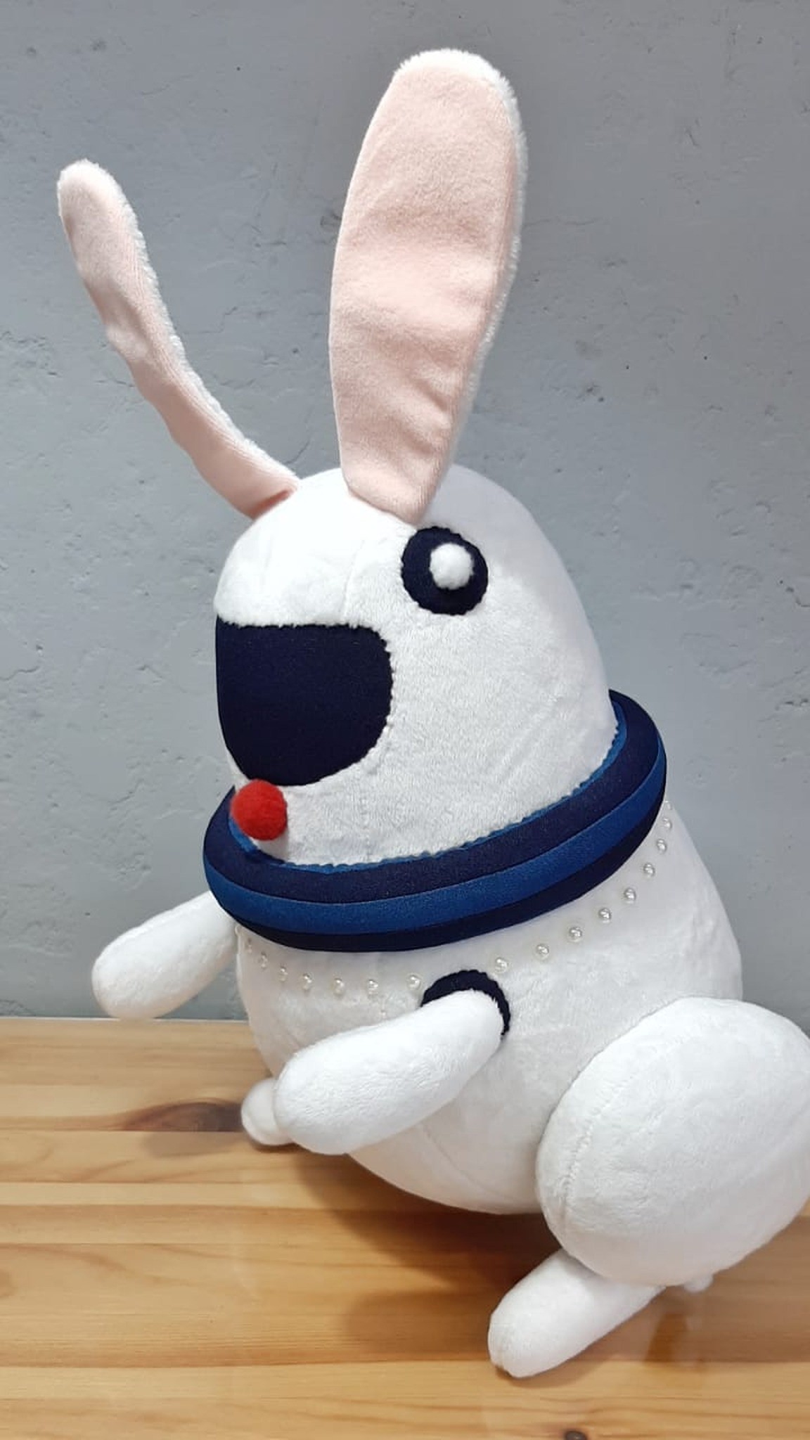 White robot bunny plush with a red pompom nose and navy collar ring, sewn from a picture