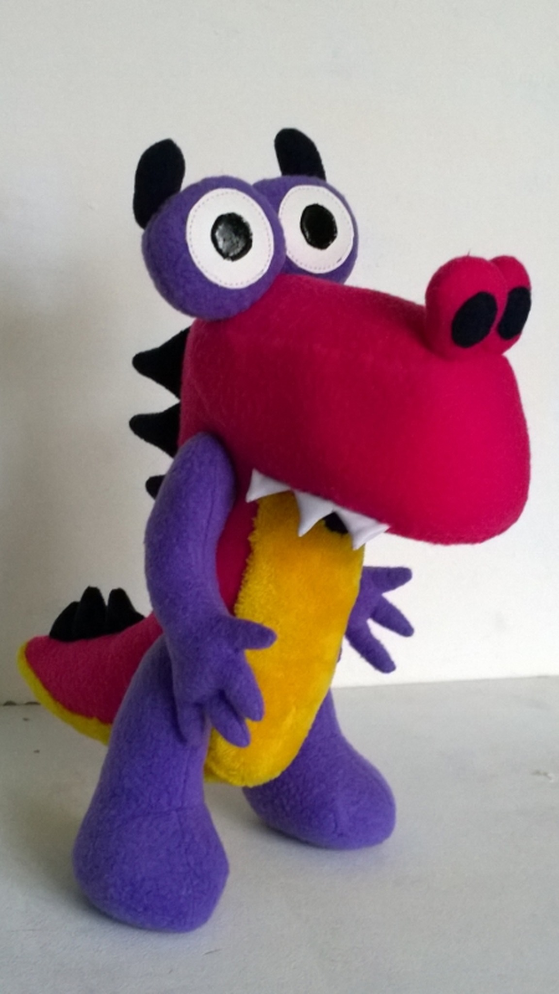 Grisha from Zavriki as a dinosaur plush standing on big purple feet, pink body, black spikes, made to order