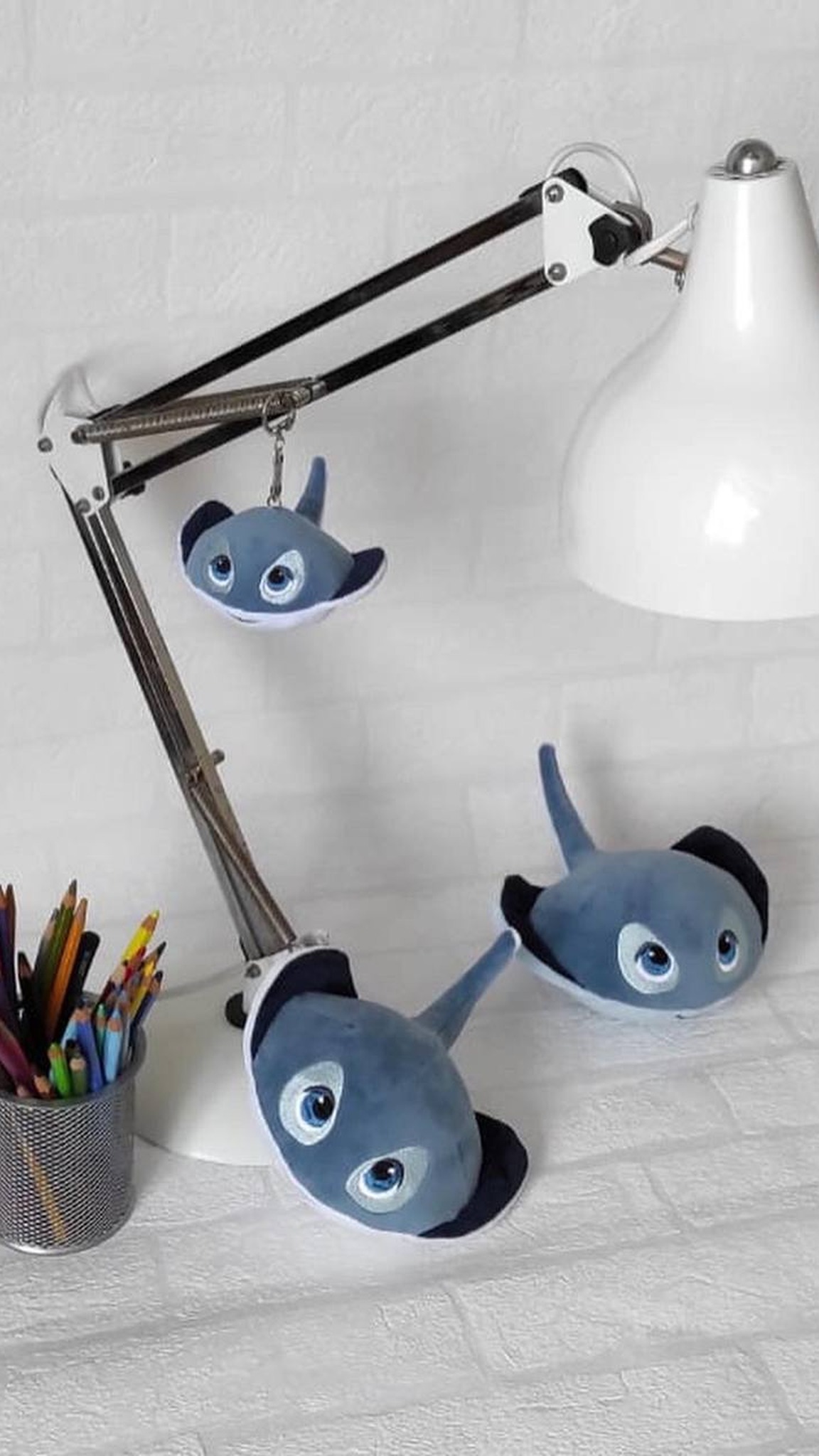 Stingray plush keychain hanging from a desk lamp, two more rays below, handmade corporate gift to order