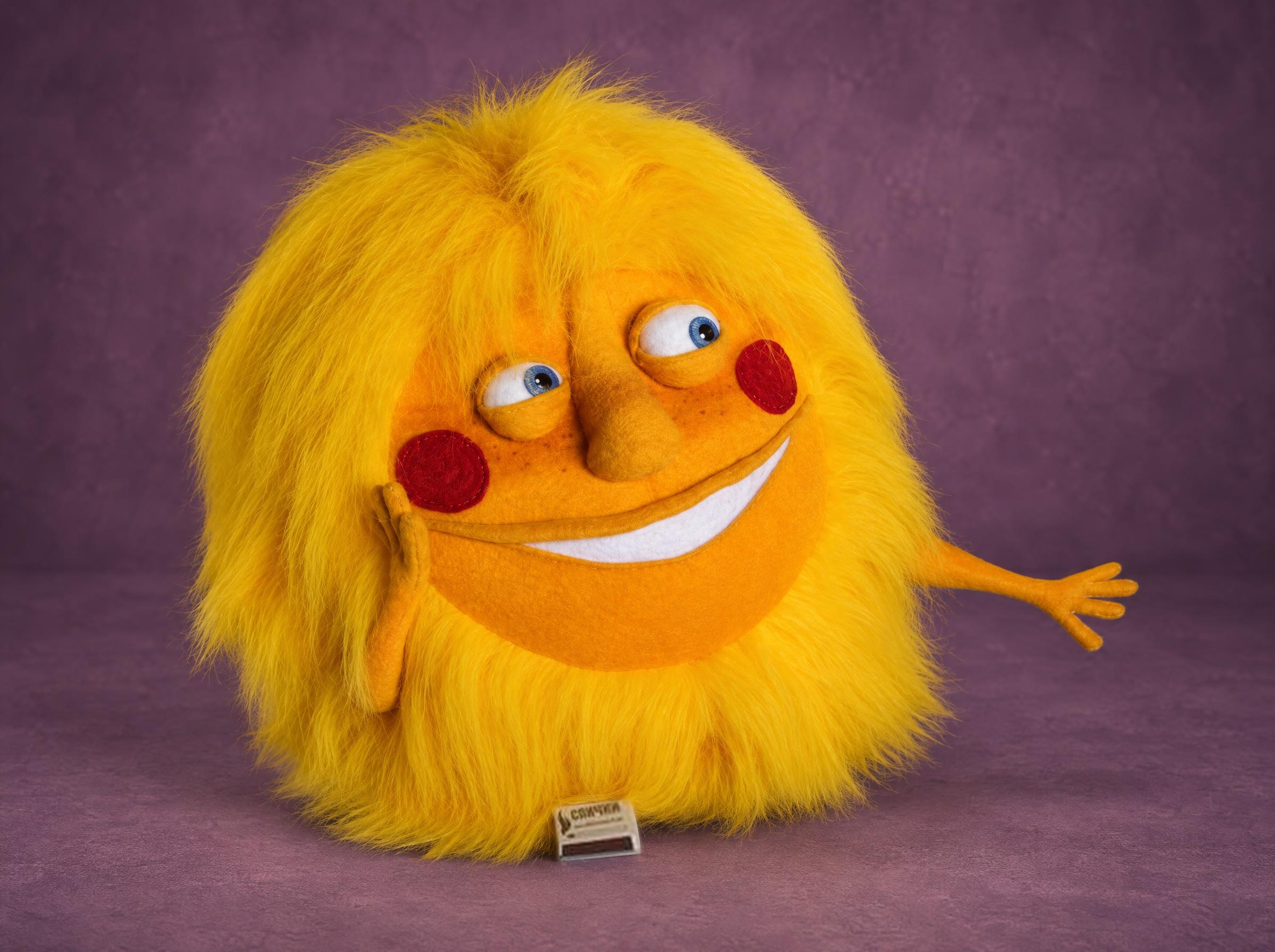Sun plush with a face, handmade to order: long yellow faux fur mane, red cheeks, white grin, one hand waving