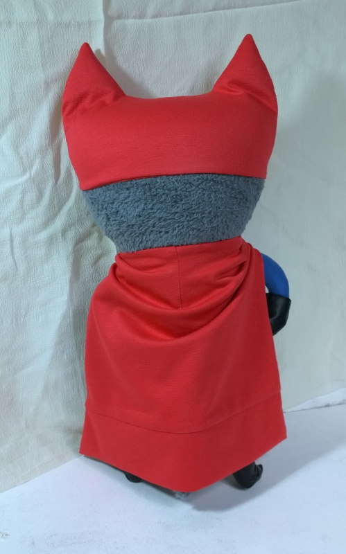 Superhero cat plush with red cape Cat superhero plush with a long red cape over its back and a red mask with tall ears, sewn from a drawing