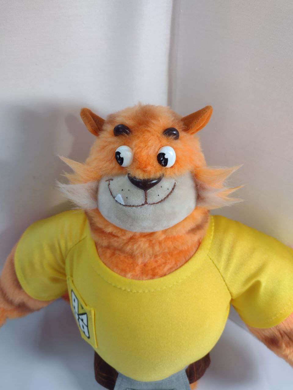 Tiger mascot plush with a cheeky grin Tiger mascot plush with a cheeky grin and one tooth, broad shoulders in a yellow T-shirt, handmade to order
