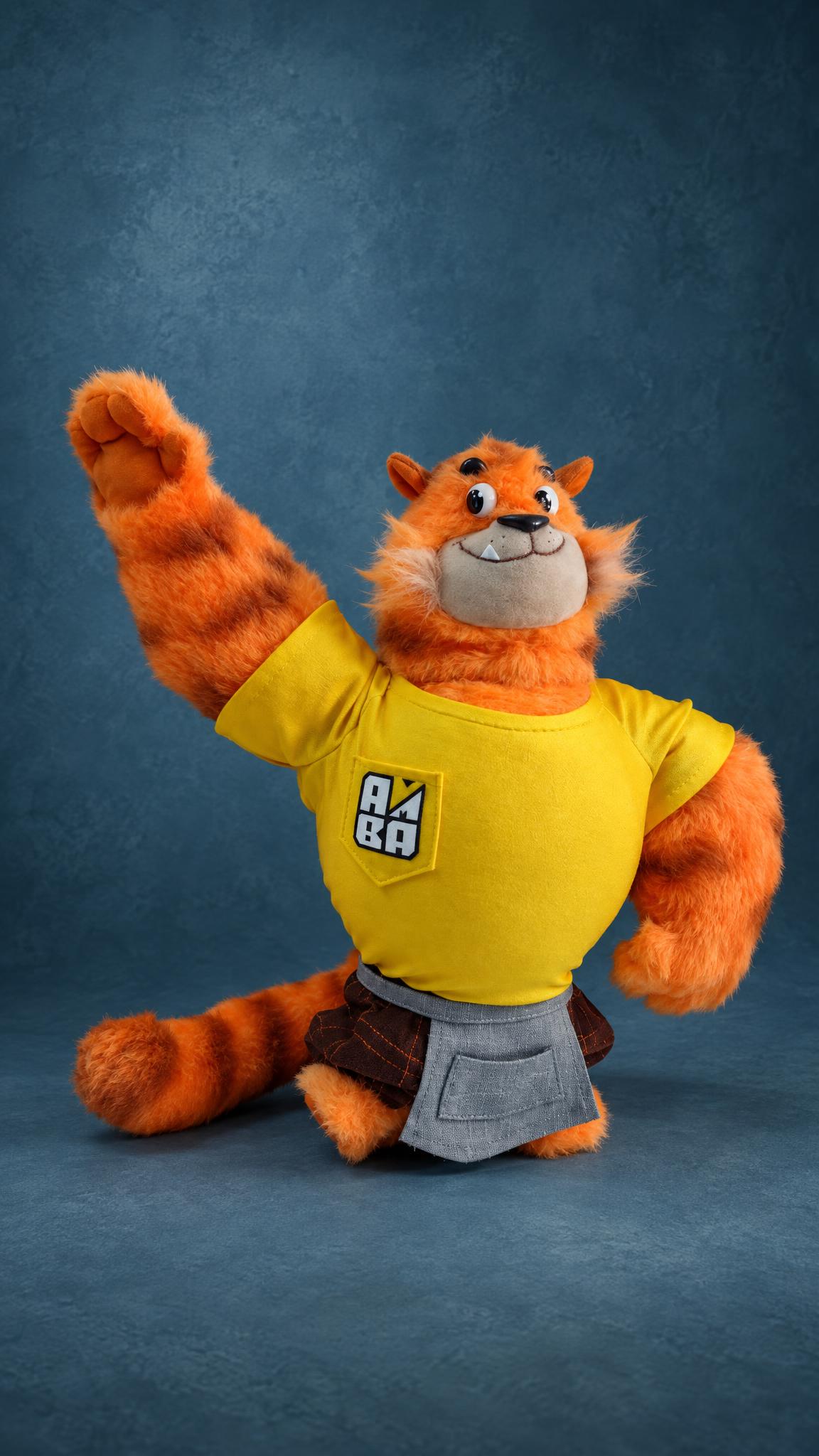 Custom tiger cat mascot plush with a raised paw, yellow T-shirt and long striped tail, sewn by hand to order
