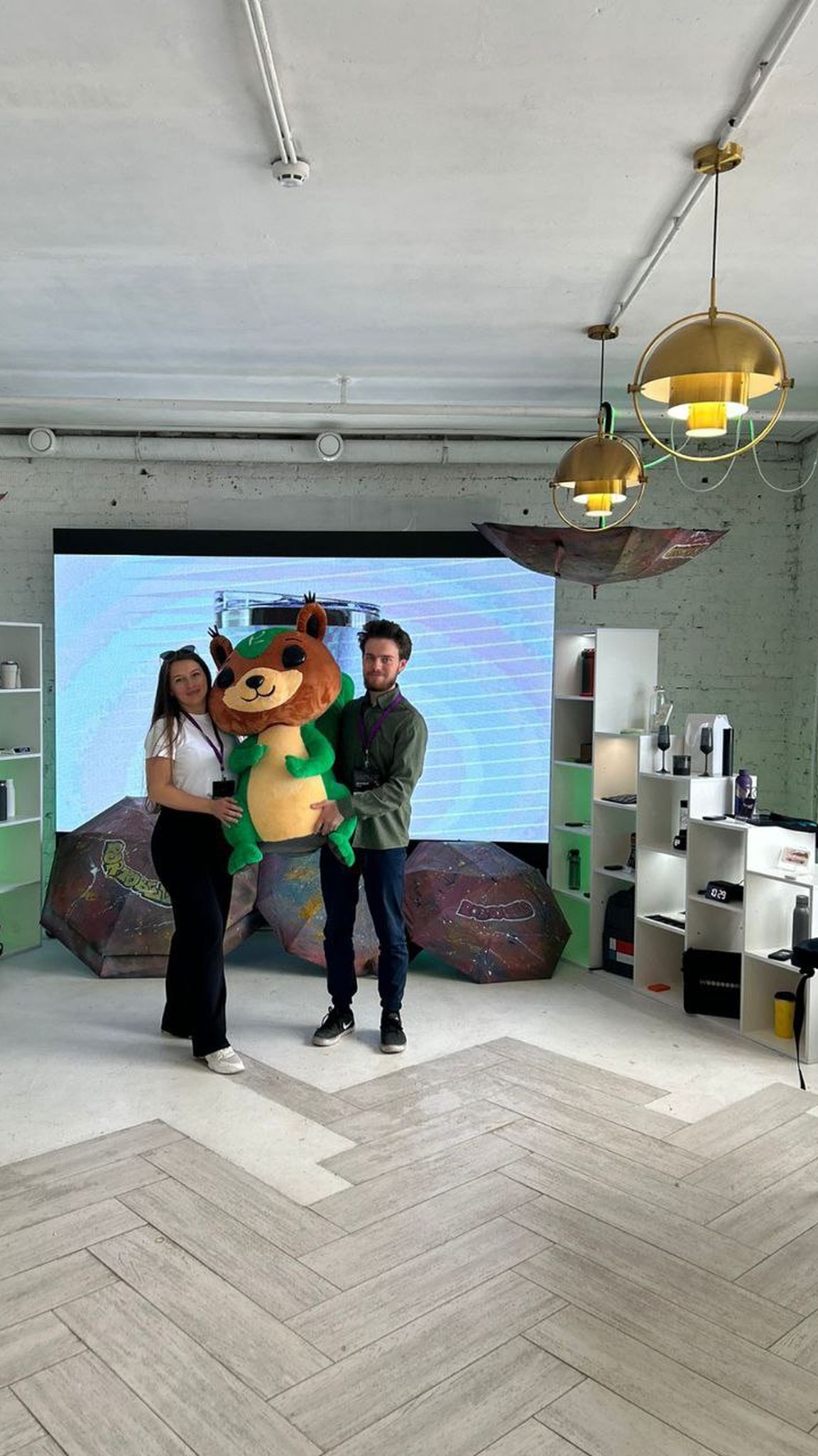 People posing with a squirrel mascot plush at an exhibition booth, a custom company mascot made to order