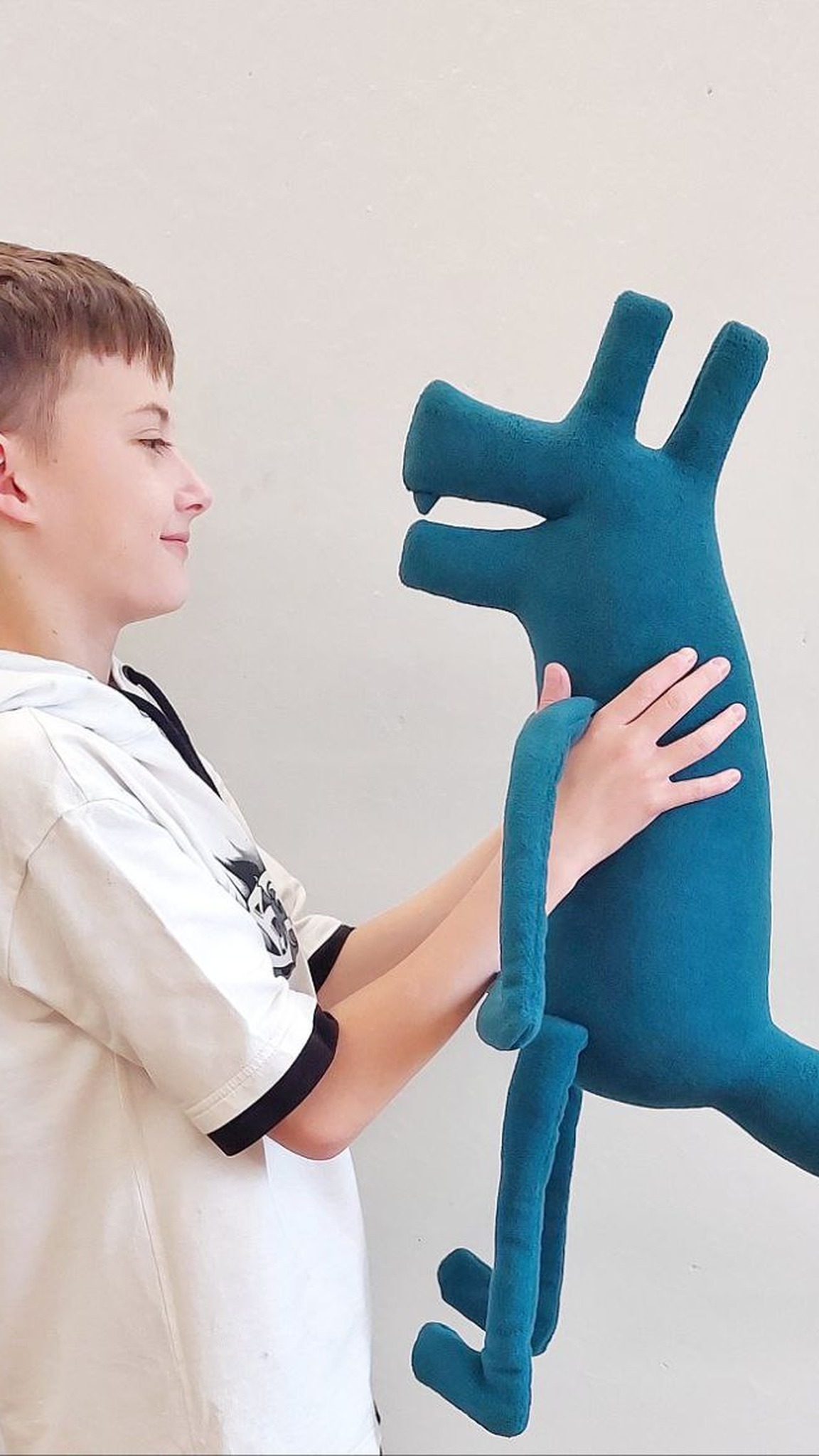 Boy smiling at the teal logo plush dog he holds, upright ears and open jaw, custom vet clinic mascot made to order