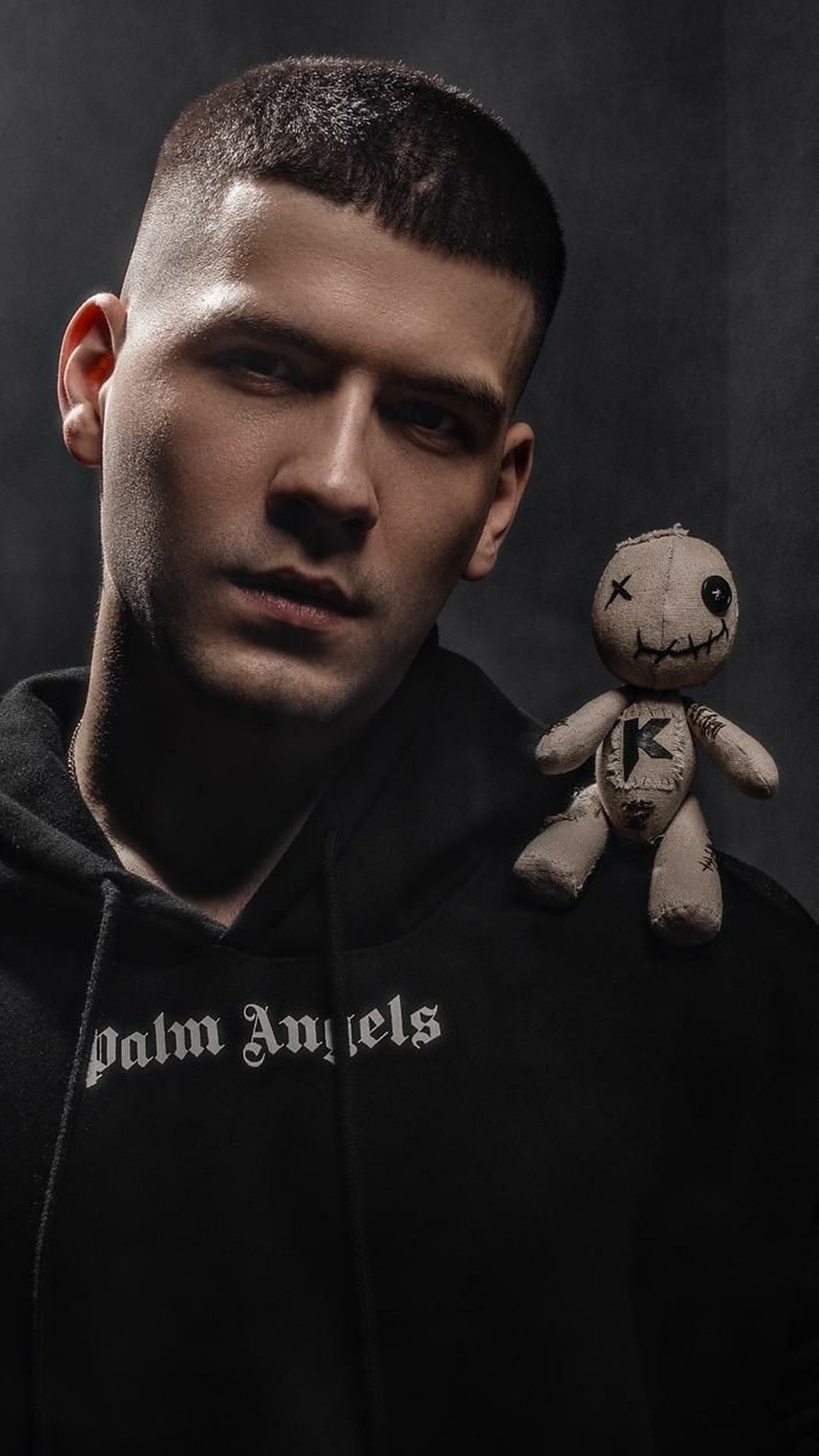 Custom voodoo doll merch with a button eye and K patch on a performer shoulder, sewn by hand to order