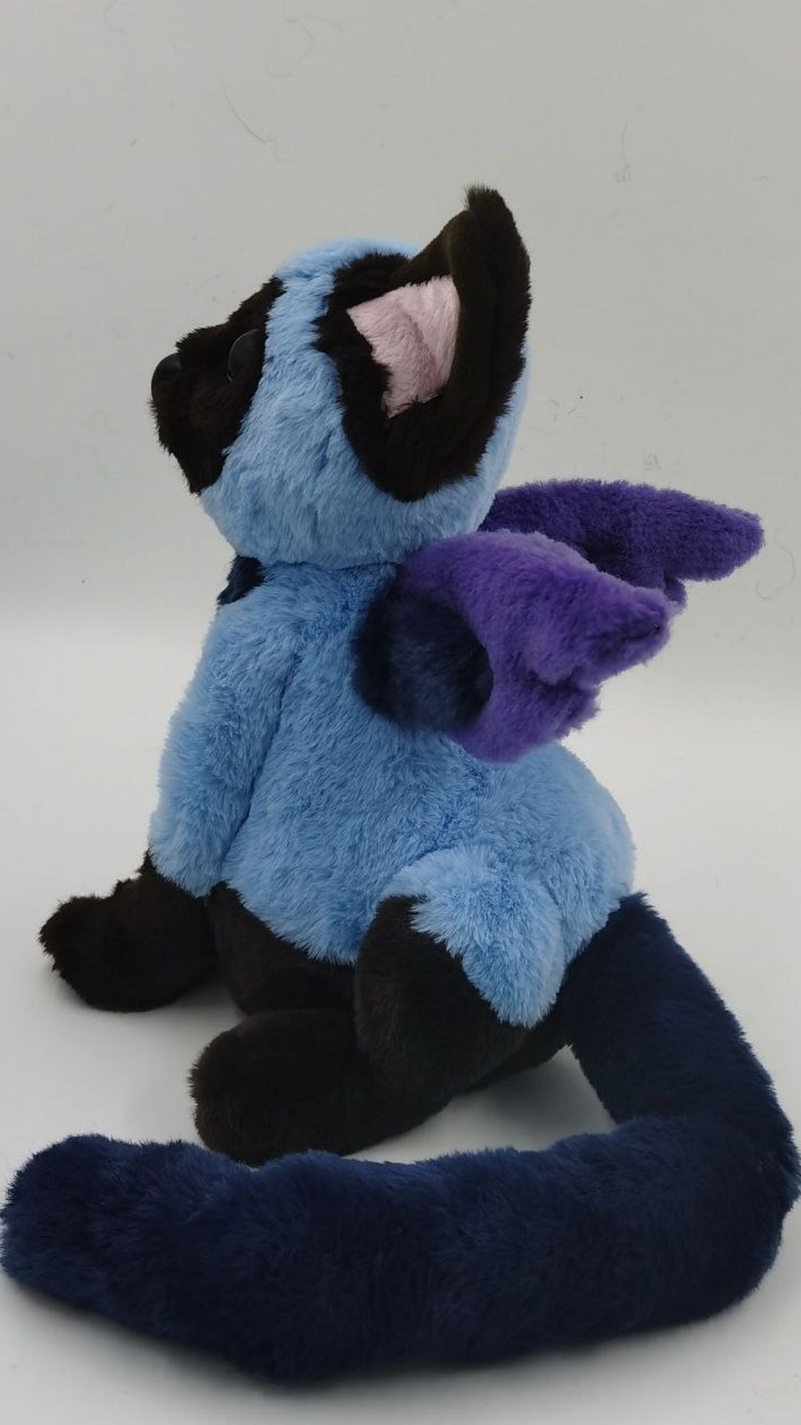 Winged cat plush with a long navy tail and purple wings on a blue back, custom made to order from a drawing