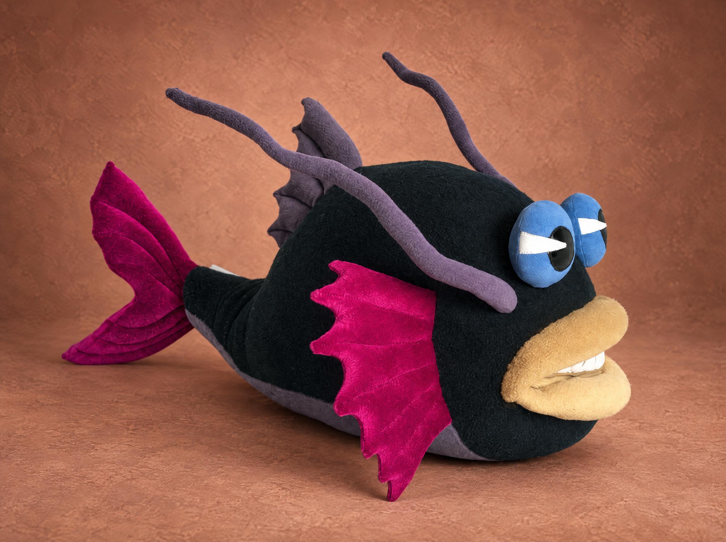 Custom fish plush made to order from a drawing: black body, magenta fins, blue eyes, beige lips and teeth